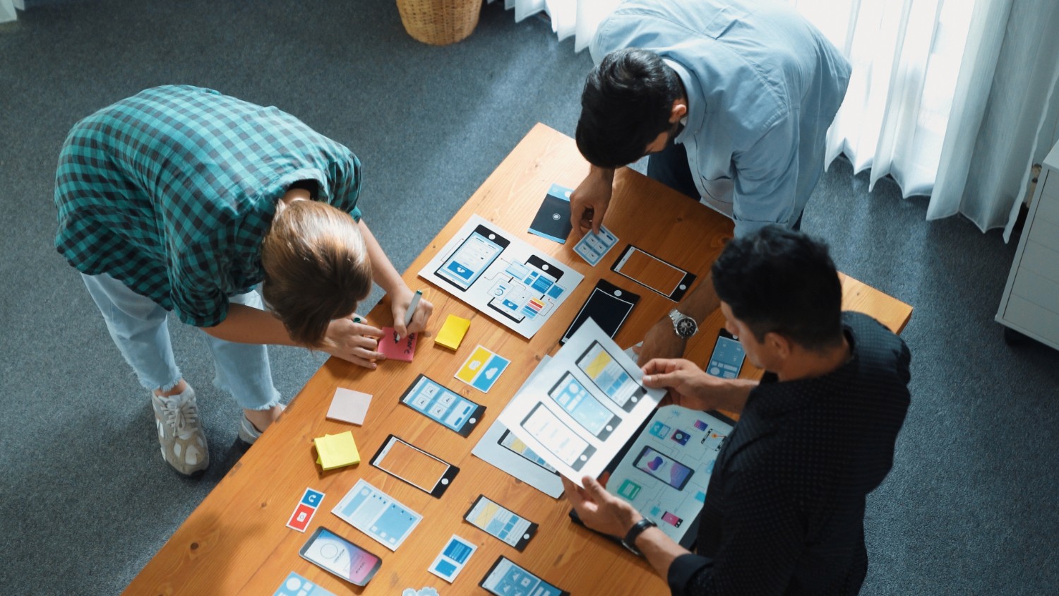 Three individuals collaborating on a laptop in a modern meeting room, engaged in discussion and teamwork.