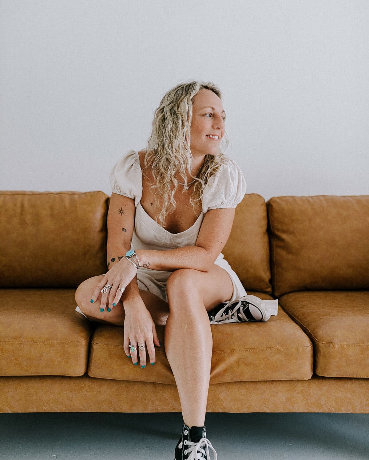 Natalie Parnell seated on a stylish couch in the bright and modern Revelator Studio, a natural light photography studio in Shreveport, perfect for creatives seeking a versatile space.