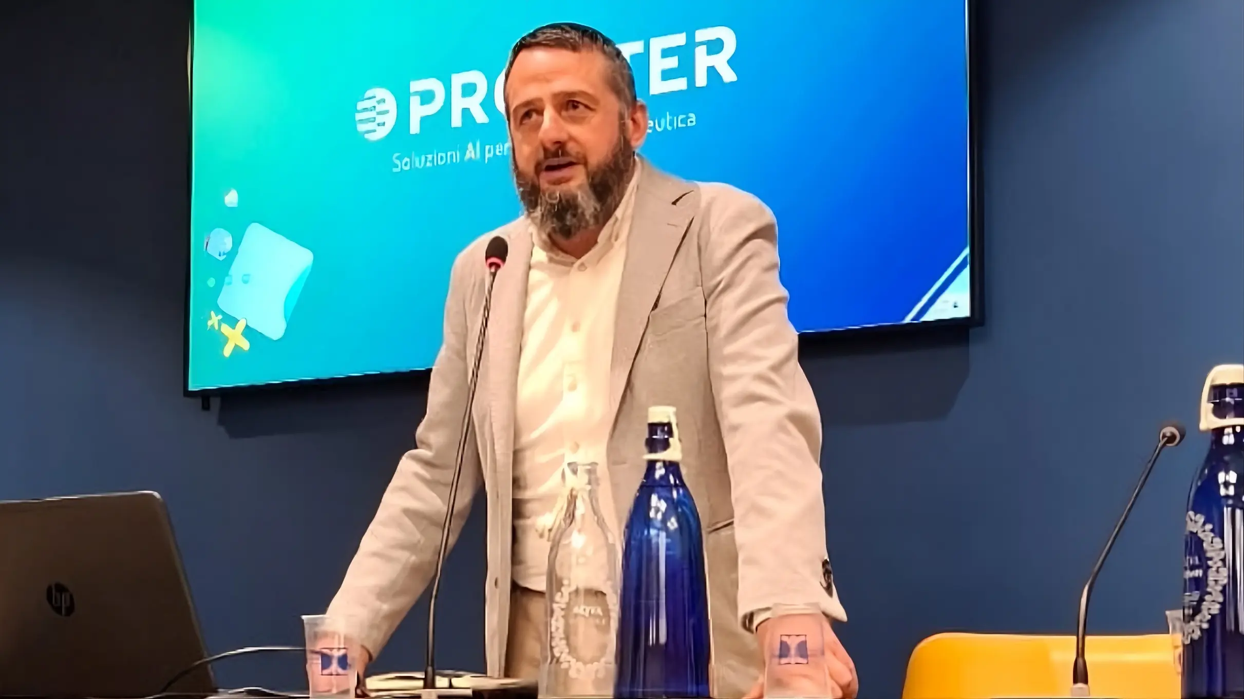 Relatore che parla al microfono durante una presentazione con il logo Profiter proiettato sullo schermo.