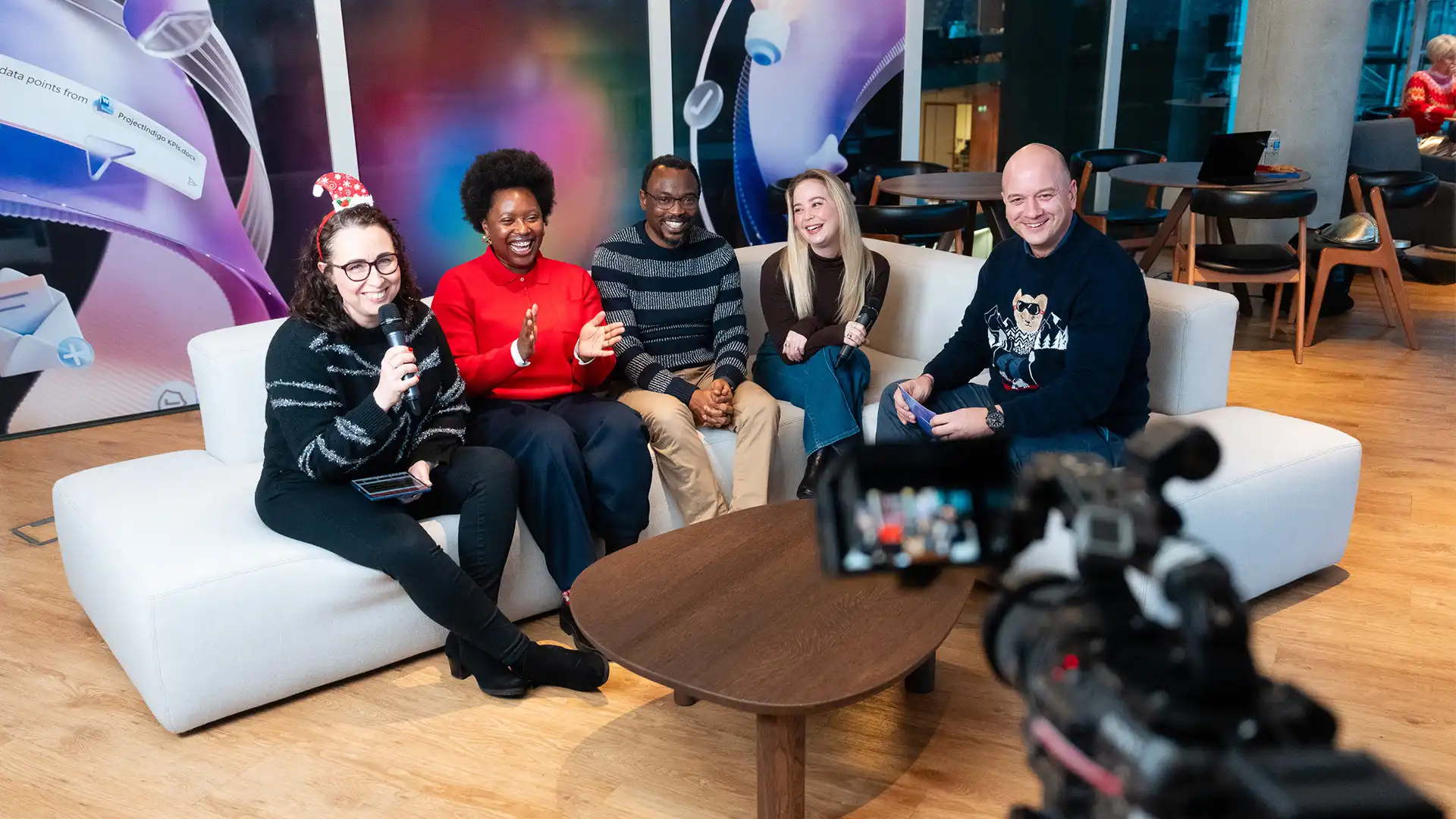 Panel-style discussion filmed for a live Microsoft broadcast, with presenters seated on a studio sofa and cameras capturing the conversation.
