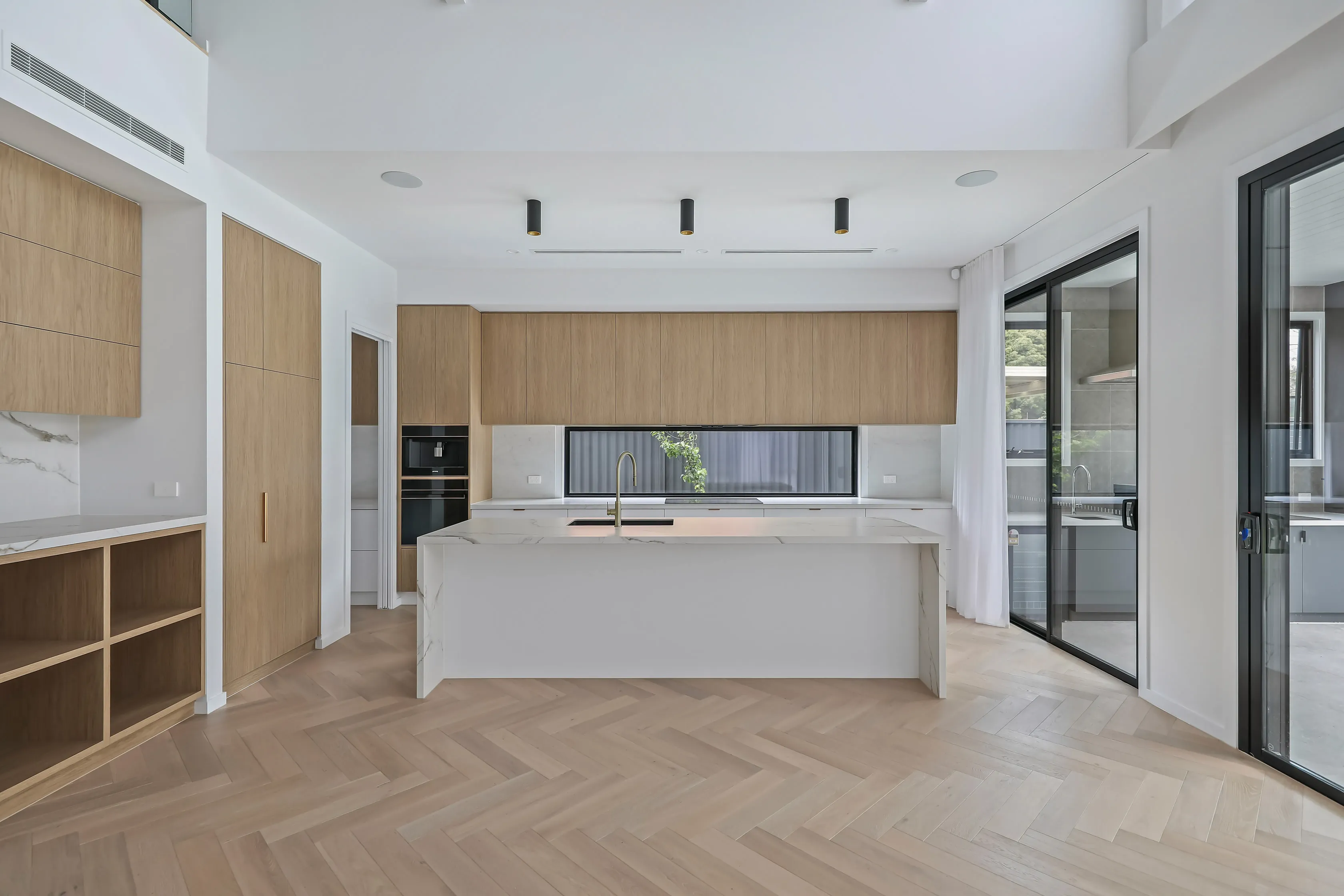 Open-plan kitchen at Mount Waverley Residence with oak cabinetry, marble-look waterfall island, brass tapware and herringbone oak floors