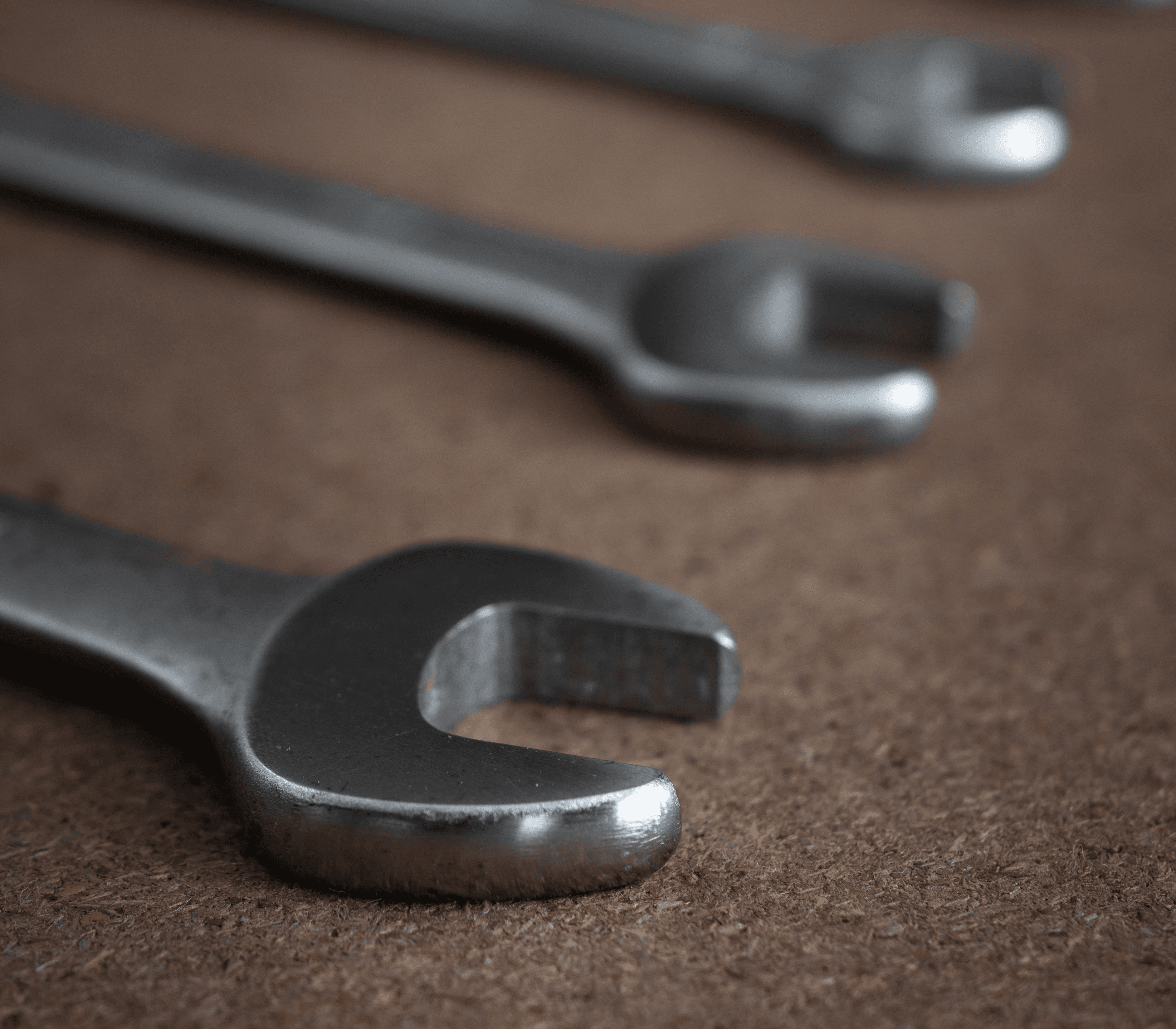 Close-up of wrenches or open end spanners lined up on a wooden board in workshop with selective focus on spanner head and background and foreground blur. Vertical orientation