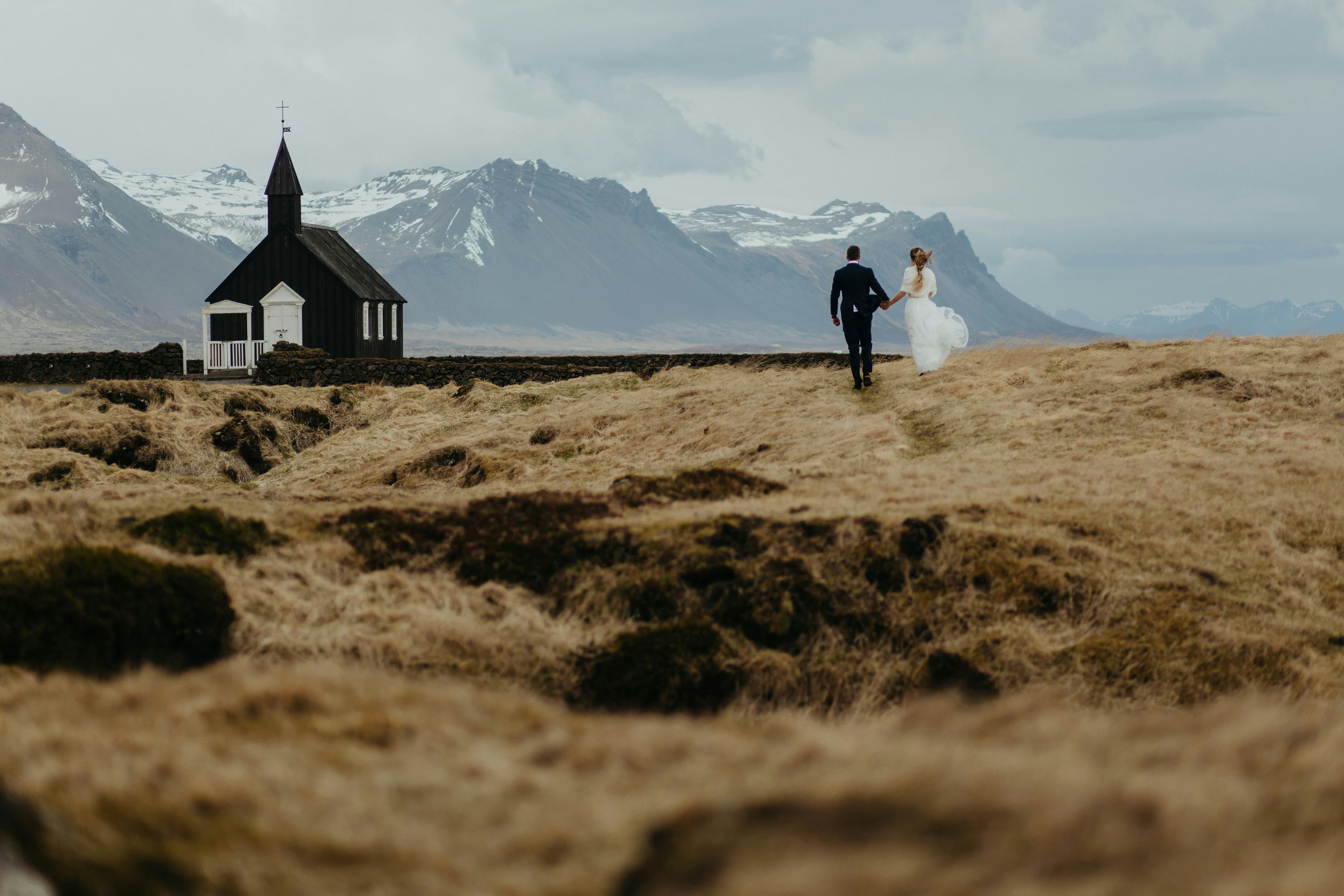 Bride and groom walking toward Búðir Black Church during fall in Iceland.