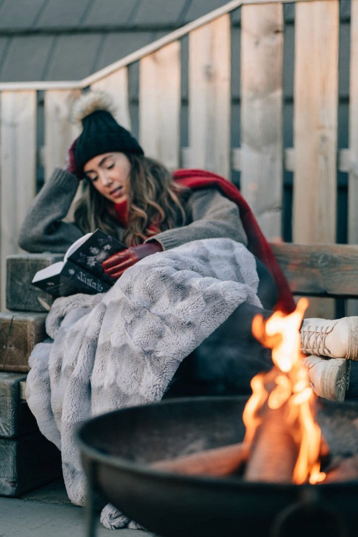 A woman reading a book in front of the fire pit.