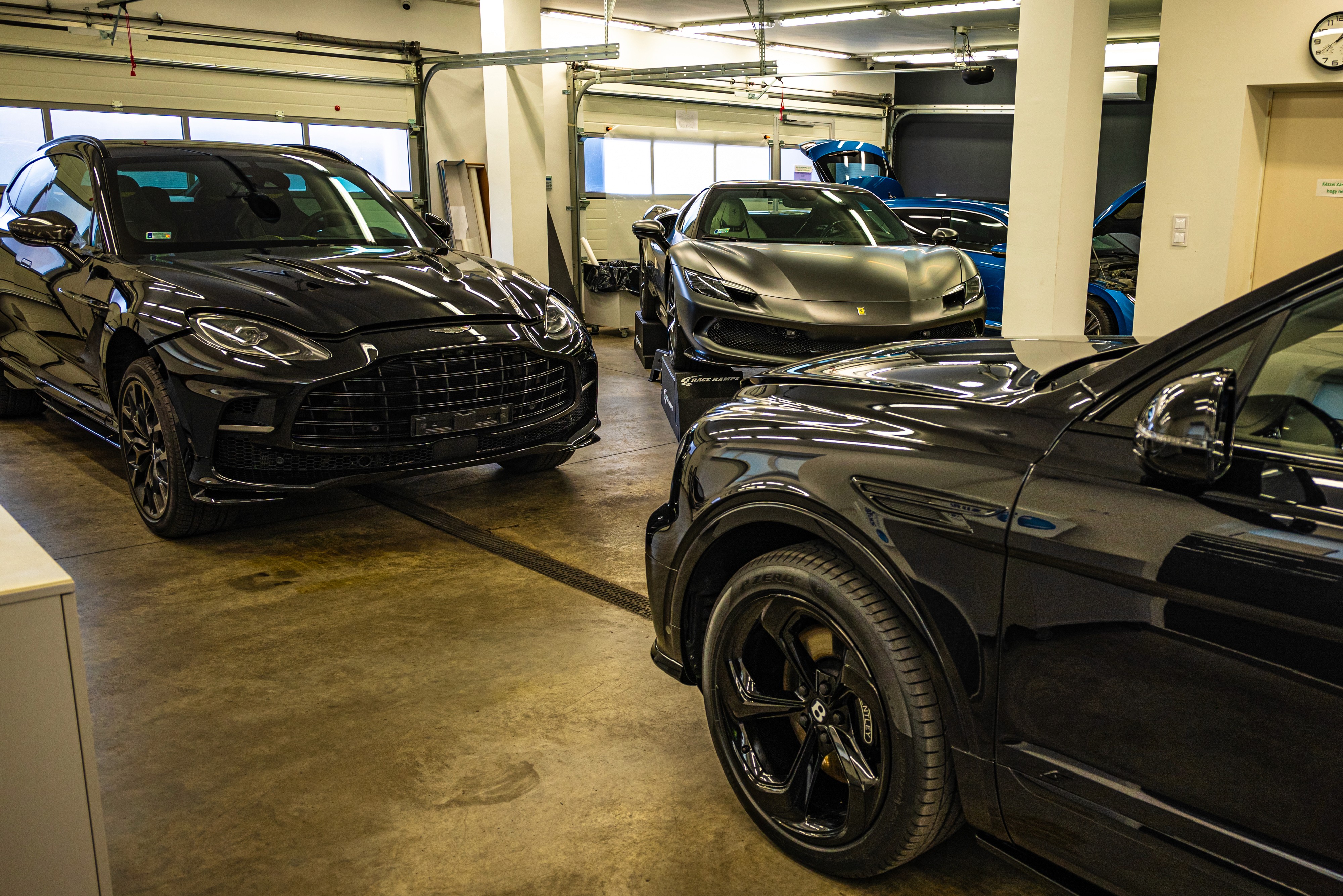 Prémium autók, köztük egy fekete Aston Martin DBX és egy matt szürke Ferrari 296GTB várnak karosszériavédő fóliázásra egy Bentayga mellett a Nortek stúdiójában.