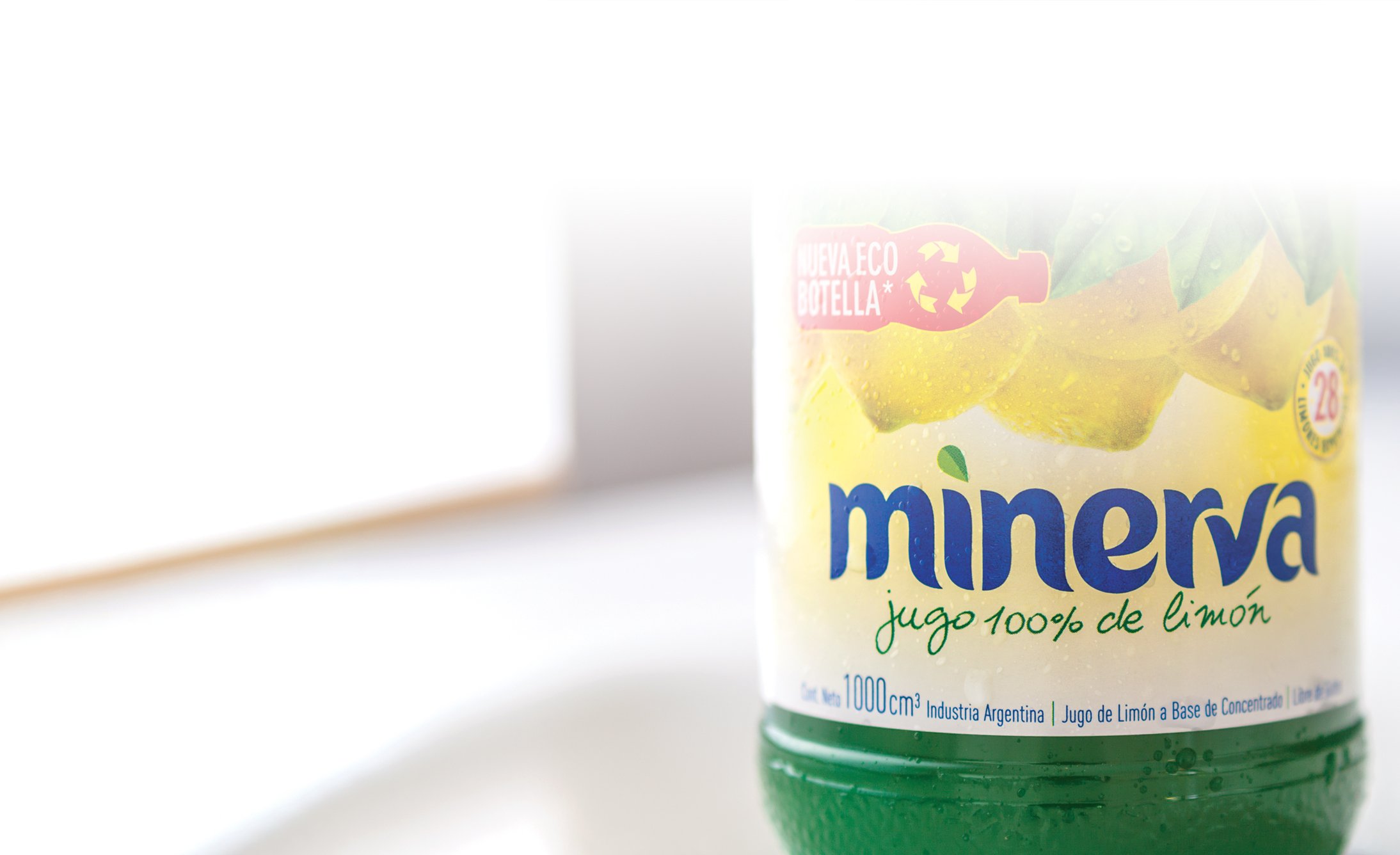 Close-up of a green Minerva lemon juice bottle with a label reading "jugo 100% de limón." The eco-friendly packaging and yellow lemon imagery are visible.