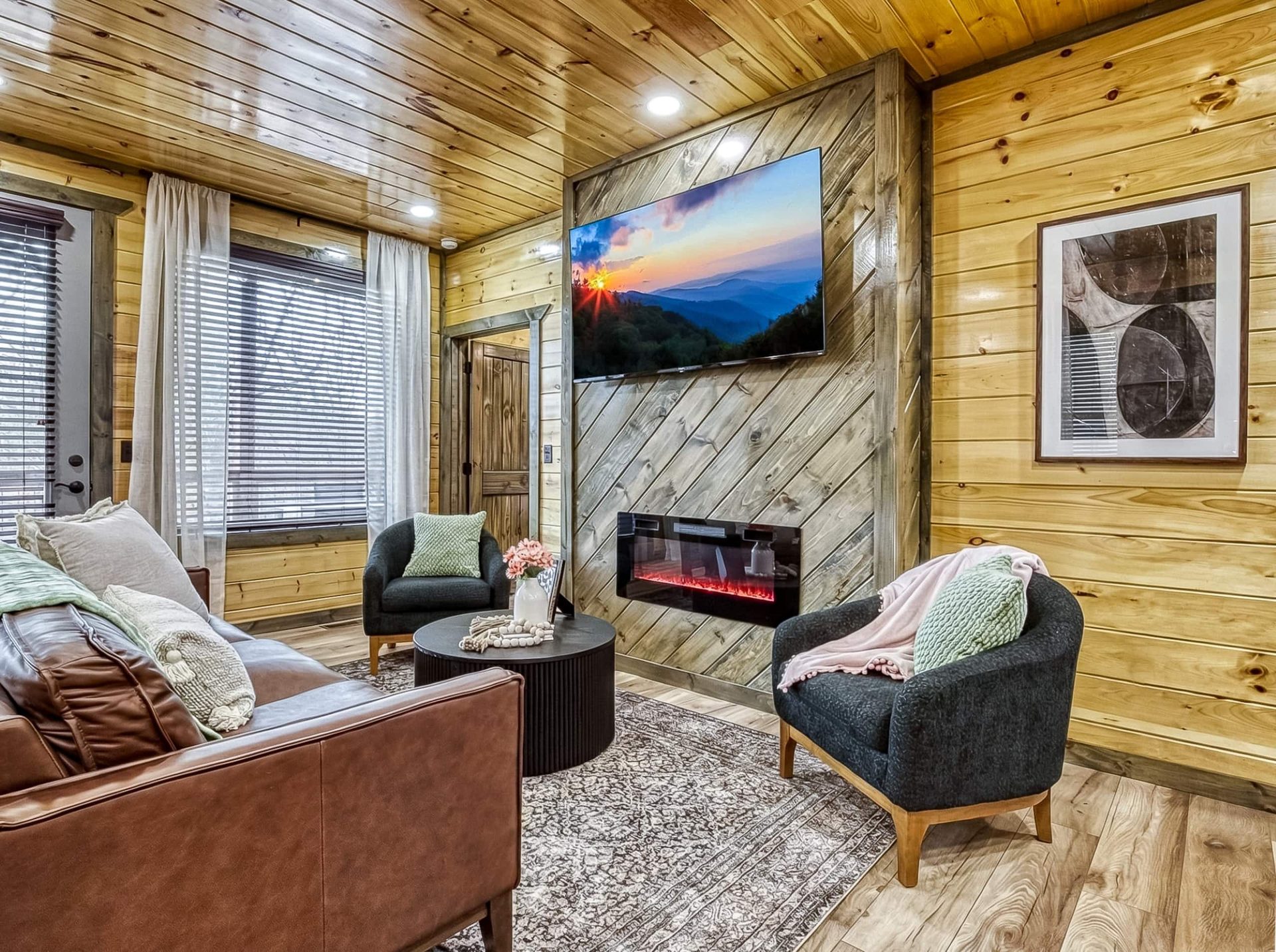 Living room with a leather sofa, two armchairs, a round coffee table and the fireplace wall, windows with sheer curtains at left