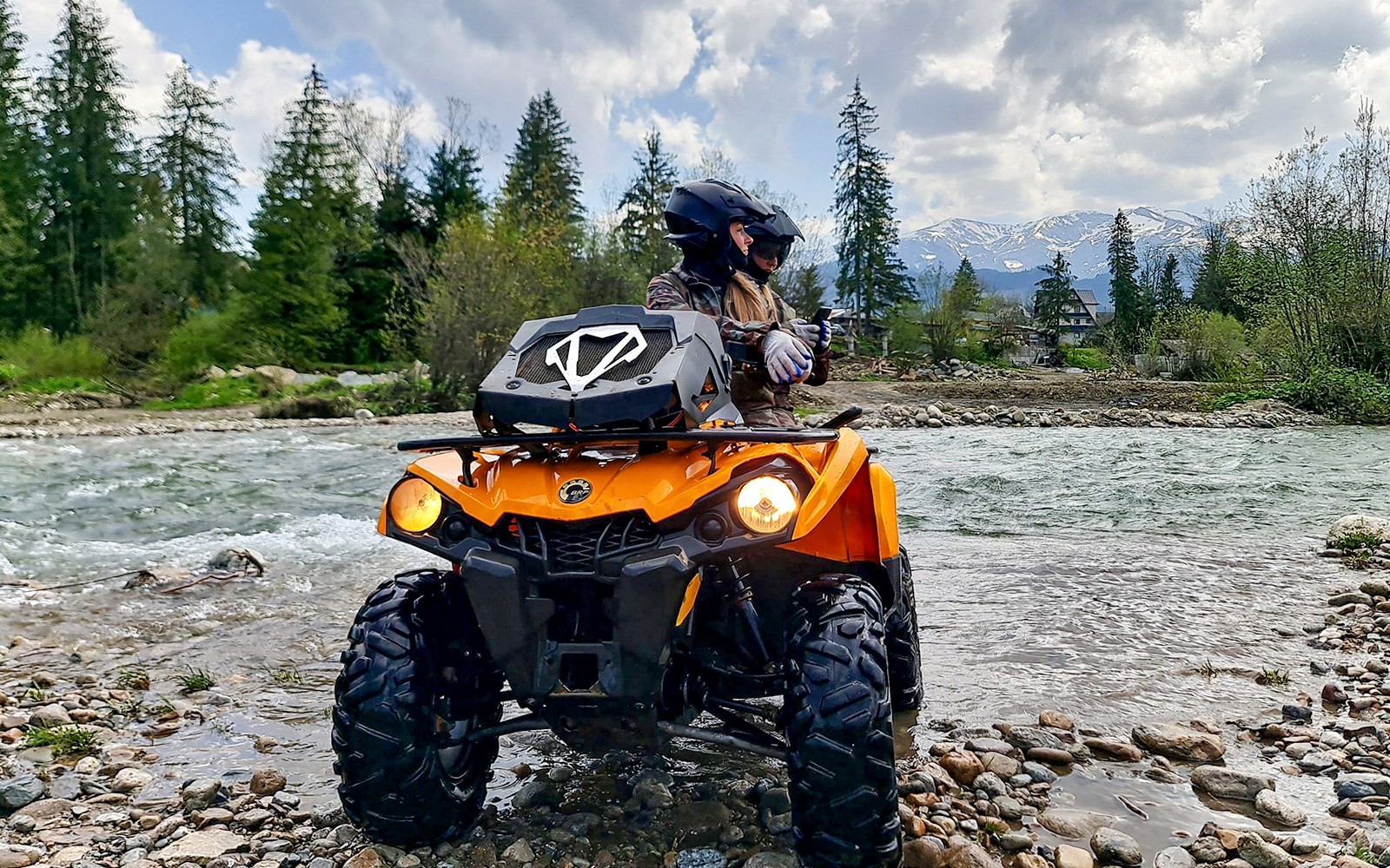 Visitors riding a quad bike by a river in Zakopane with mountains in the background.