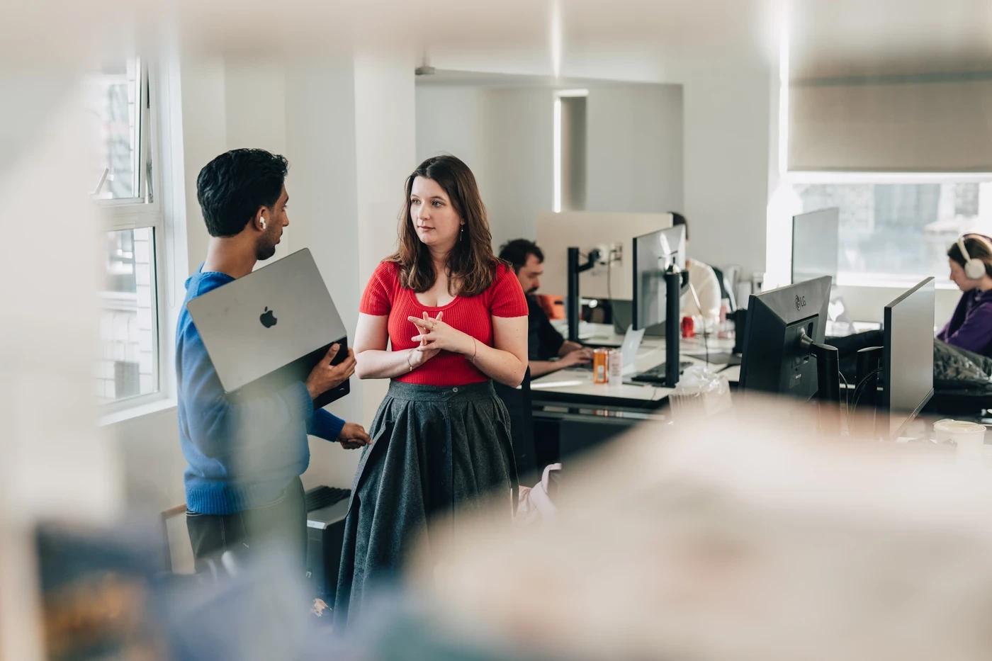 Christian Harinarain talking with a colleague beside the desks in V7’s London office, holding an open laptop
