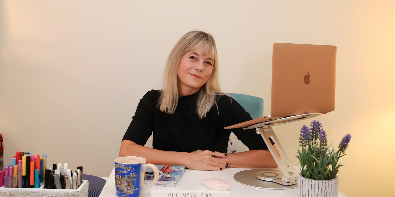 Kori Burkholder, Career Clarity and Reinvention Coach, sitting at her desk with a laptop, pens, and a motivational 'YES YOU CAN' sign