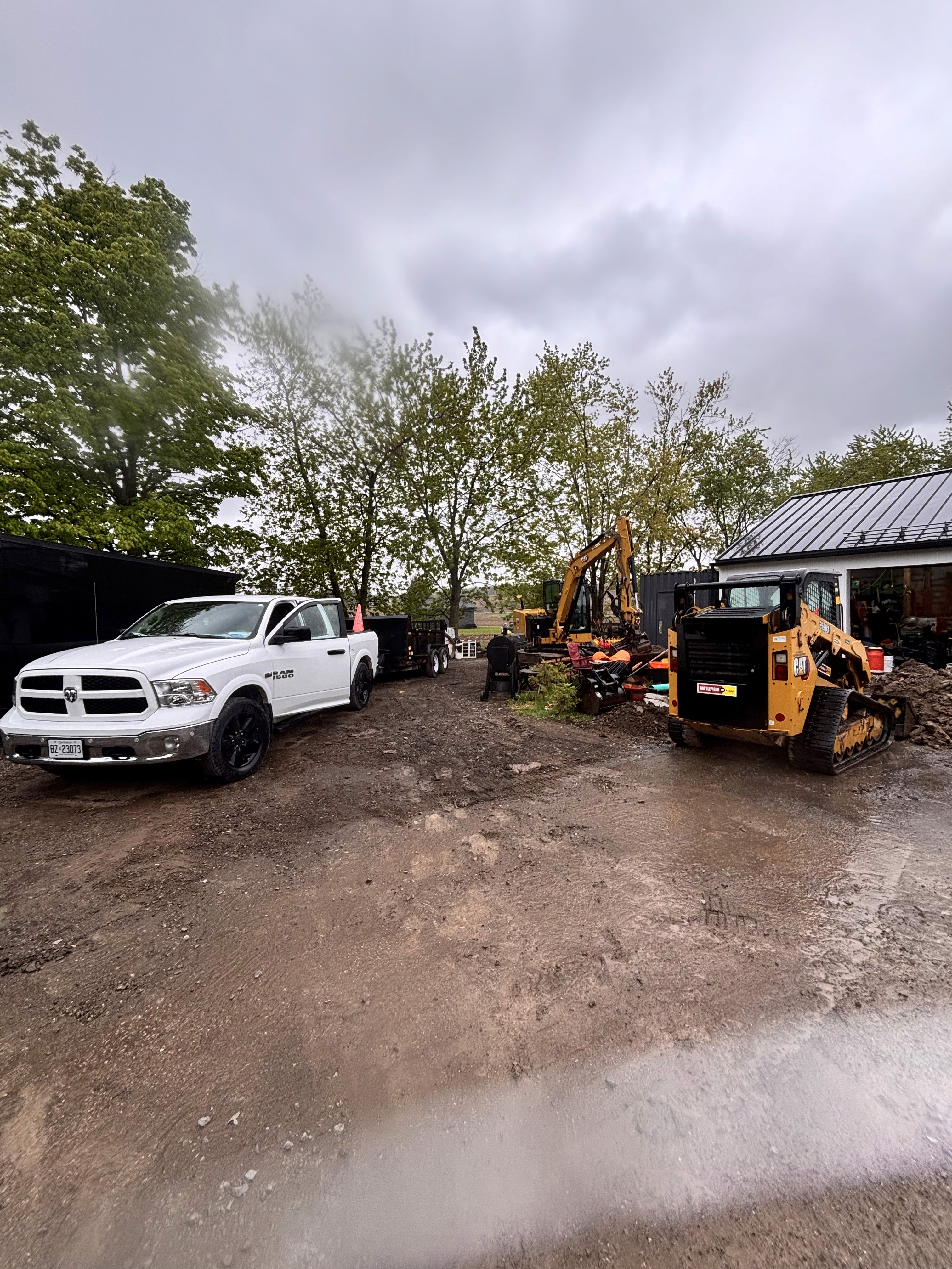 Two vehicles in a driveway, with trees and cloudy skies in the background. Wet ground suggests recent rain.