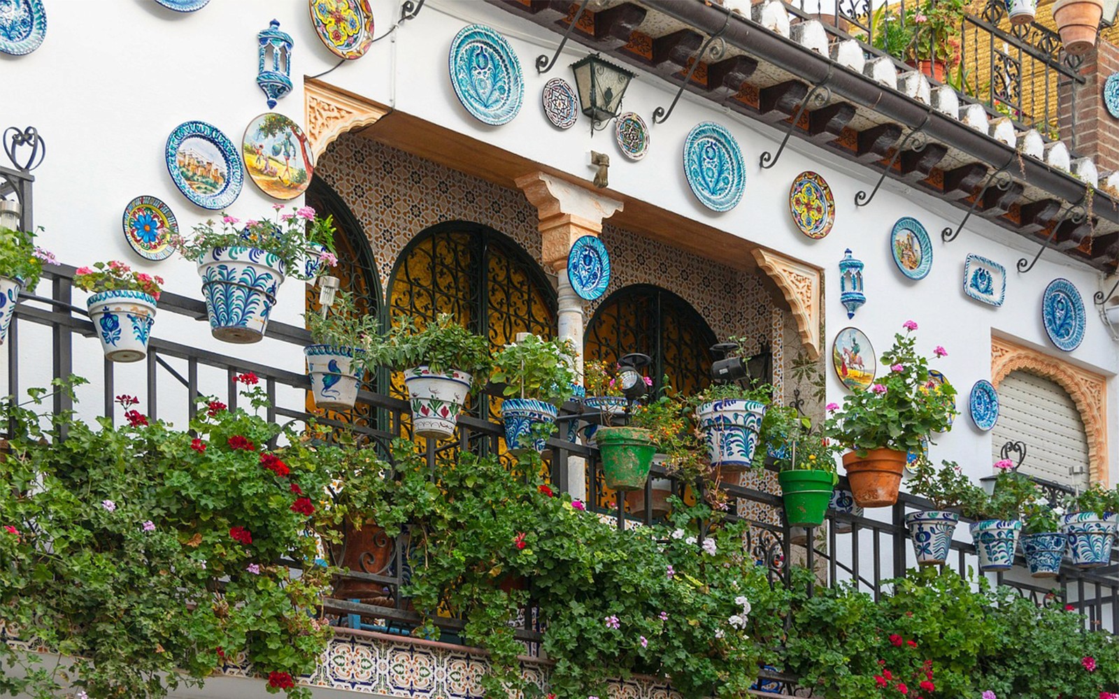 Ornate balcony with colorful ceramic plates and potted plants in Granada, Alhambra.
