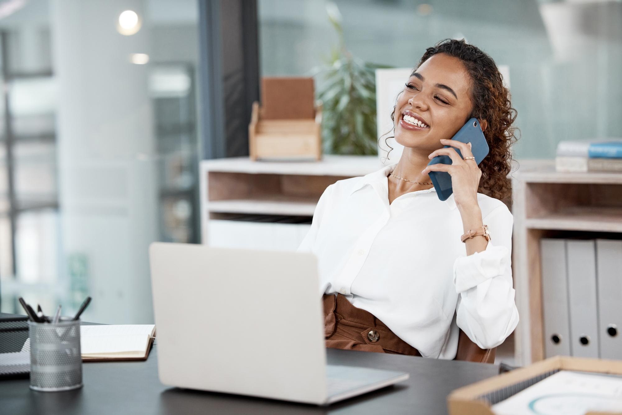 Zakenvrouw blij aan de telefoon met laptop op bureau — AI-klantenservice voor MKB