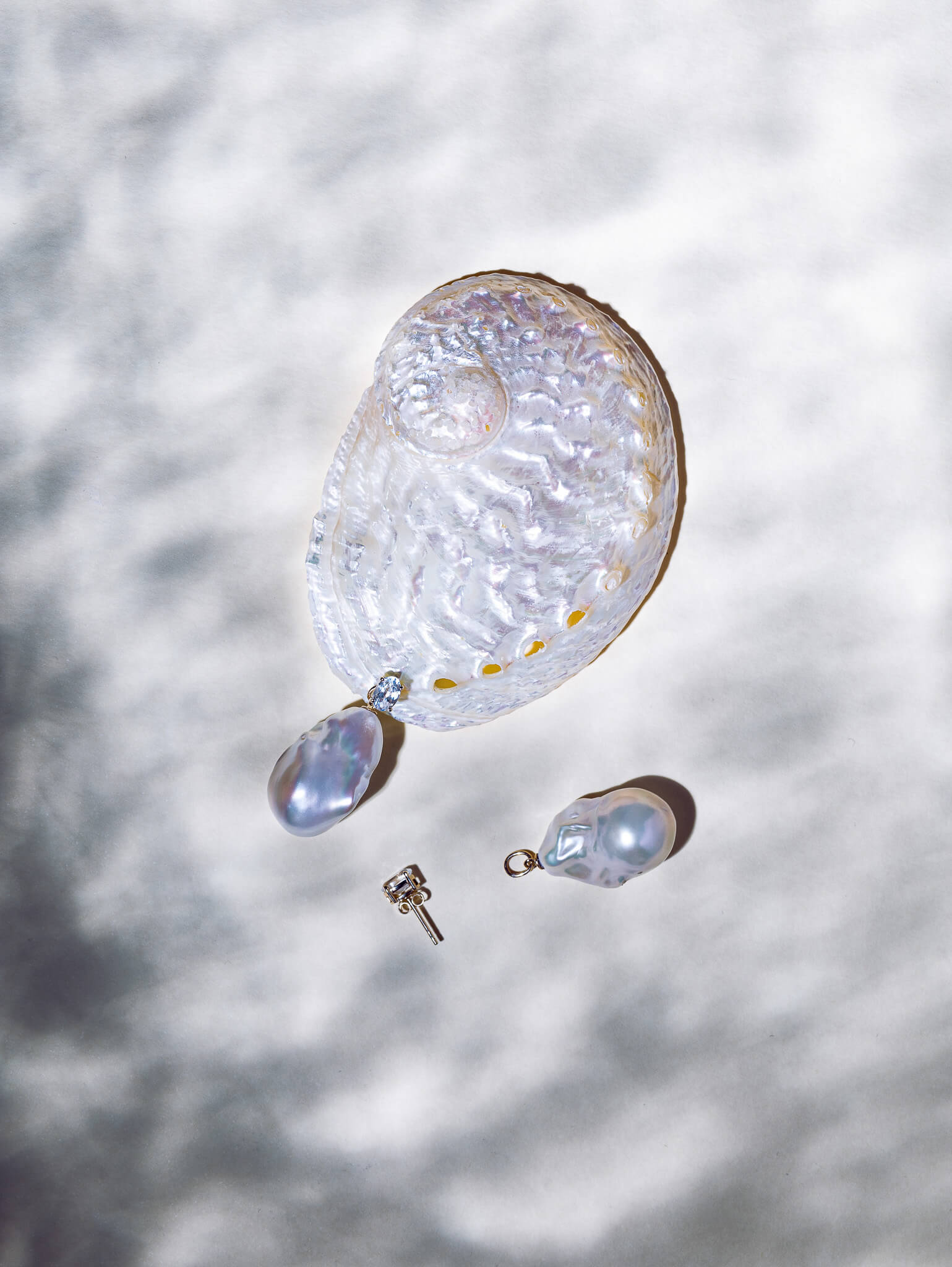 Editorial still-life photography of pearl jewellery pieces with shell texture and soft shadows.