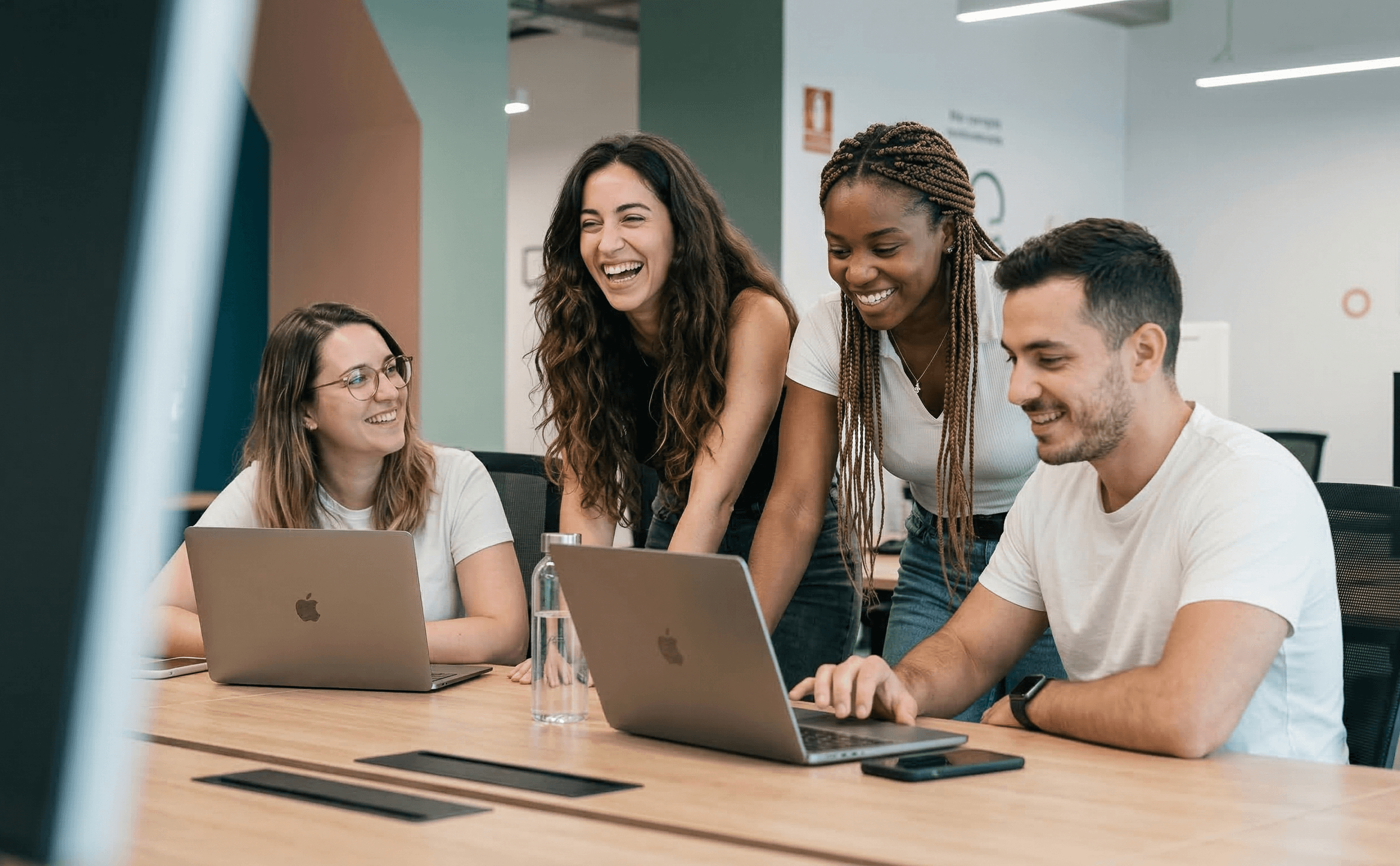 Group of coworkers collaborating and smiling around laptops