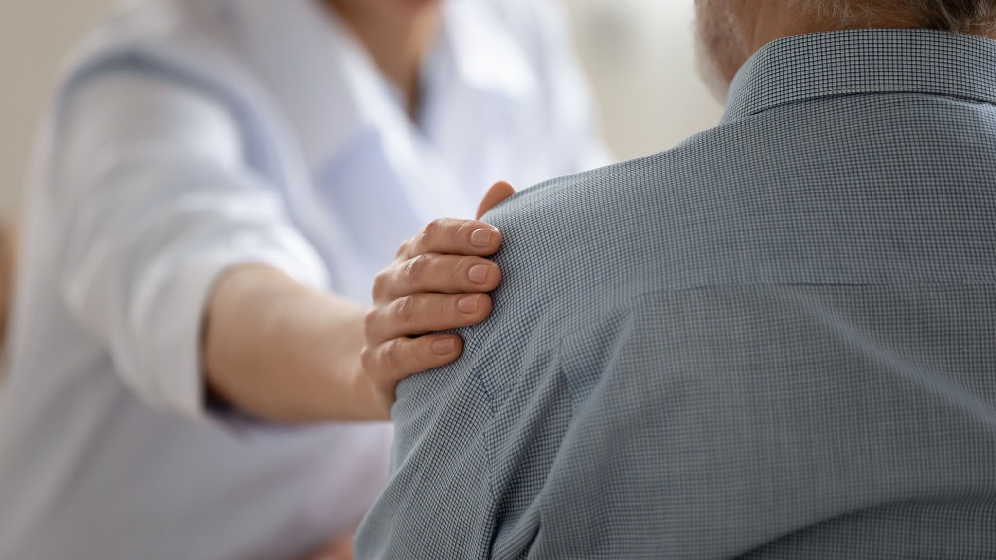 Photo of doctor placing arm on R shoulder of patient, reassuring the patient 