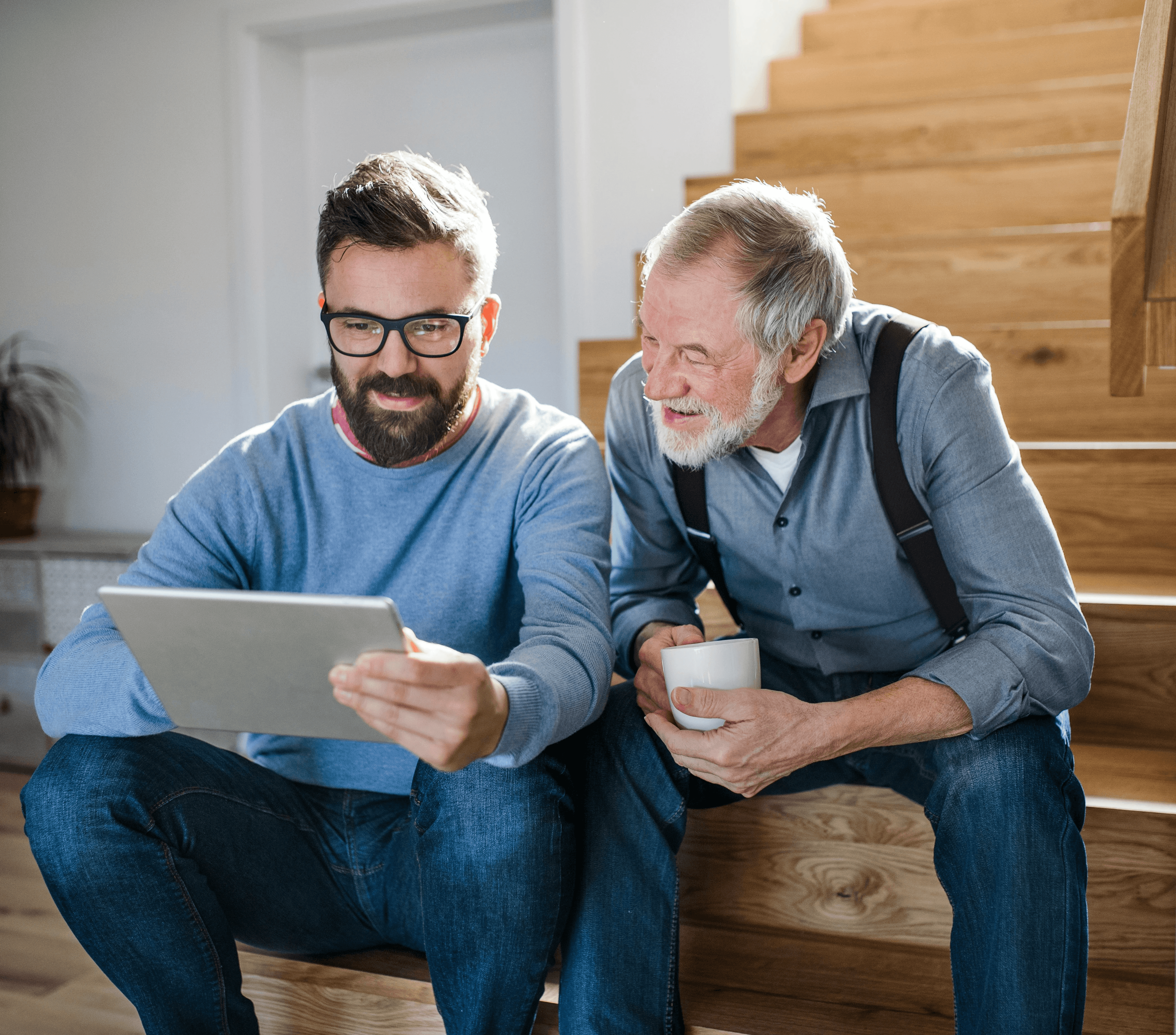 Two men sitting on a staircase, one looking at a tablet and the other holding a cup.