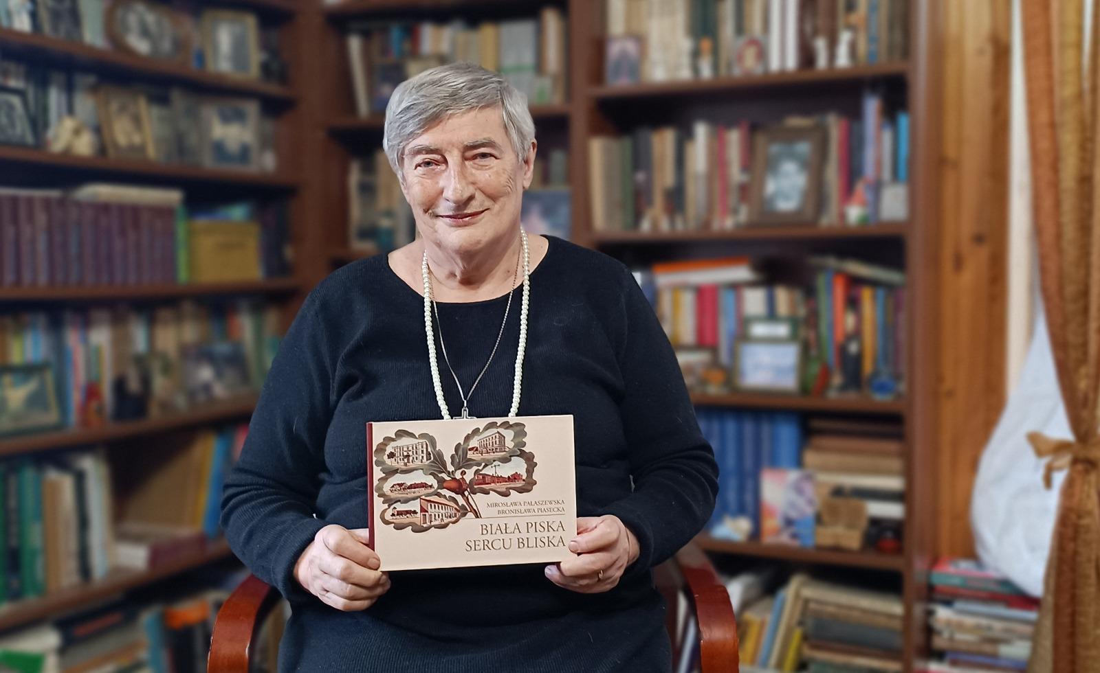 A woman with auburn hair and a gray coat over a white sweater, set against a neutral background, exuding a minimalist aesthetic.