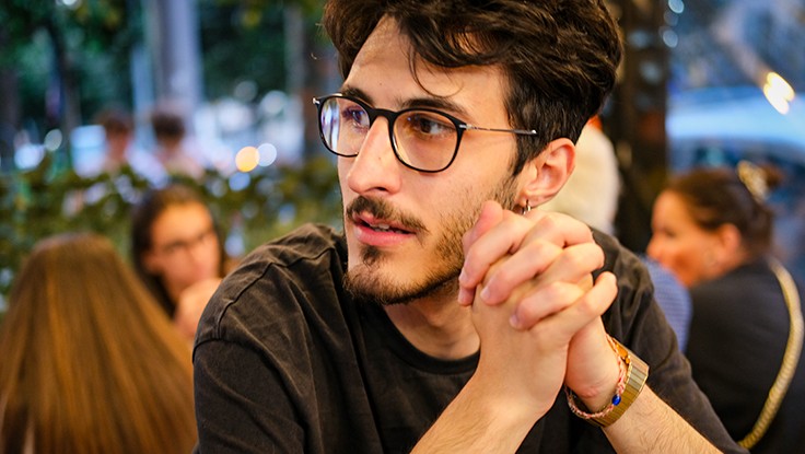 Angelo Tanzillo sitting with hands clasped, looking away in a busy café setting.
