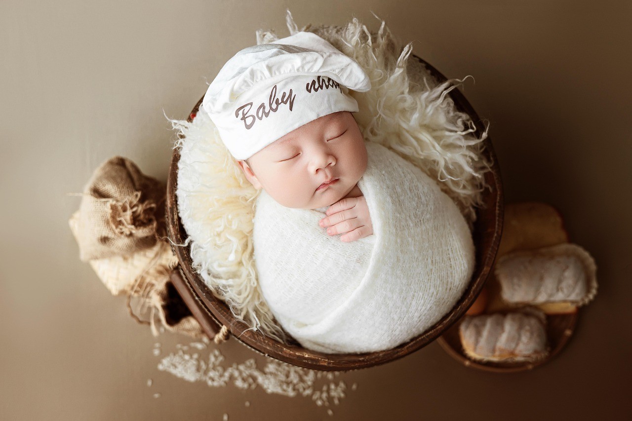 Un nouveau-né endormi enveloppé dans une couverture, portant un bonnet avec le texte "Baby".