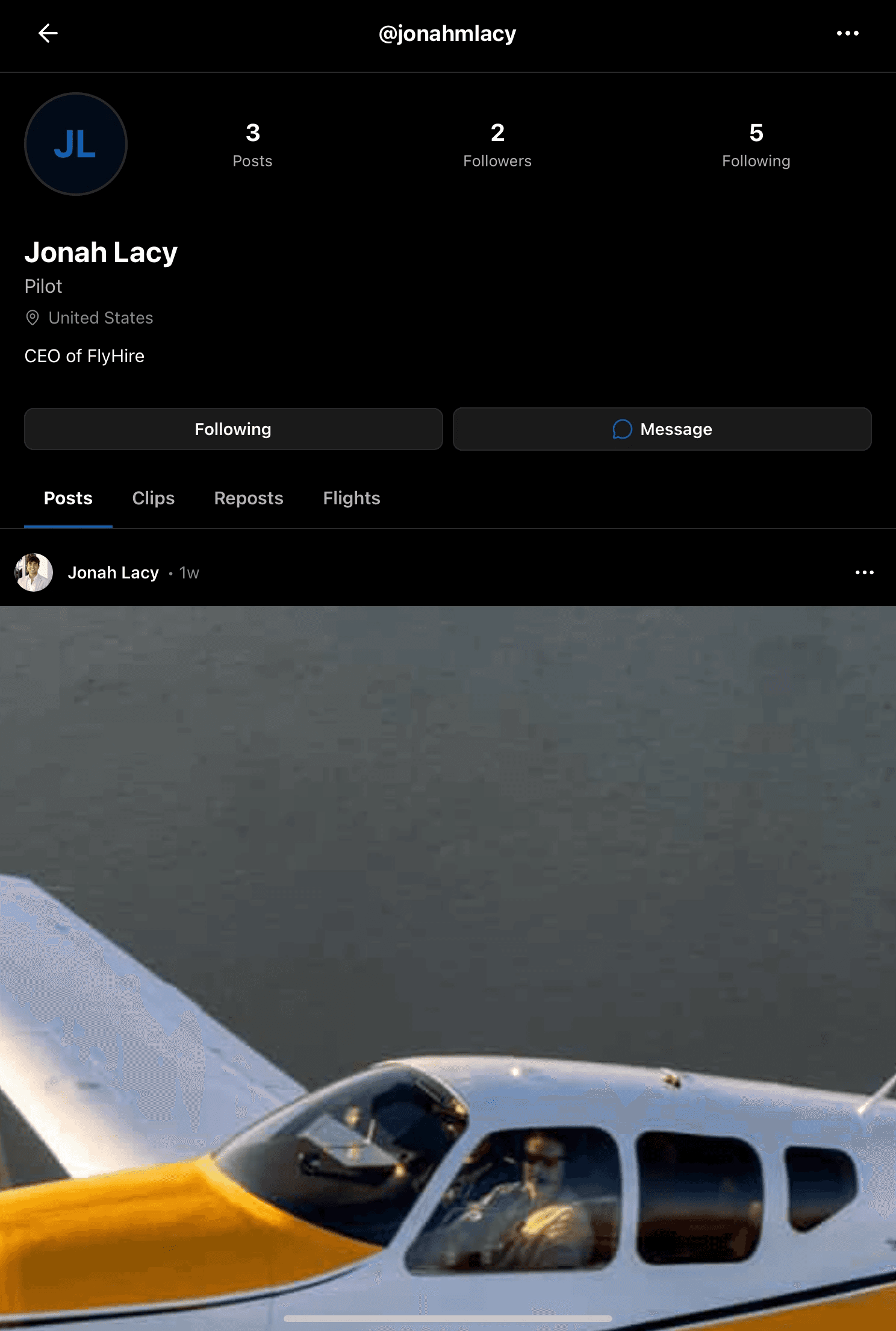 Man wearing a beige cap and dark shirt working on a laptop at a wooden desk with a plant in the background.