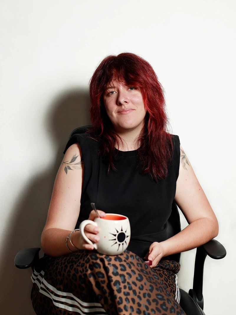 Maïlys Vial assise sur une chaise noire avec une tasse à la main.