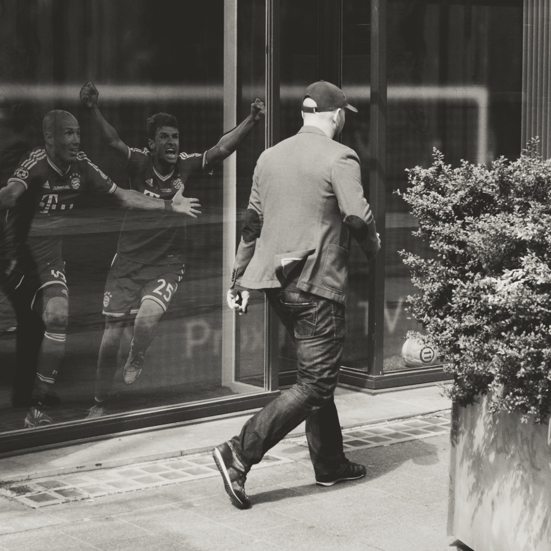 Man in suit walking past window with soccer players celebrating in background outside.