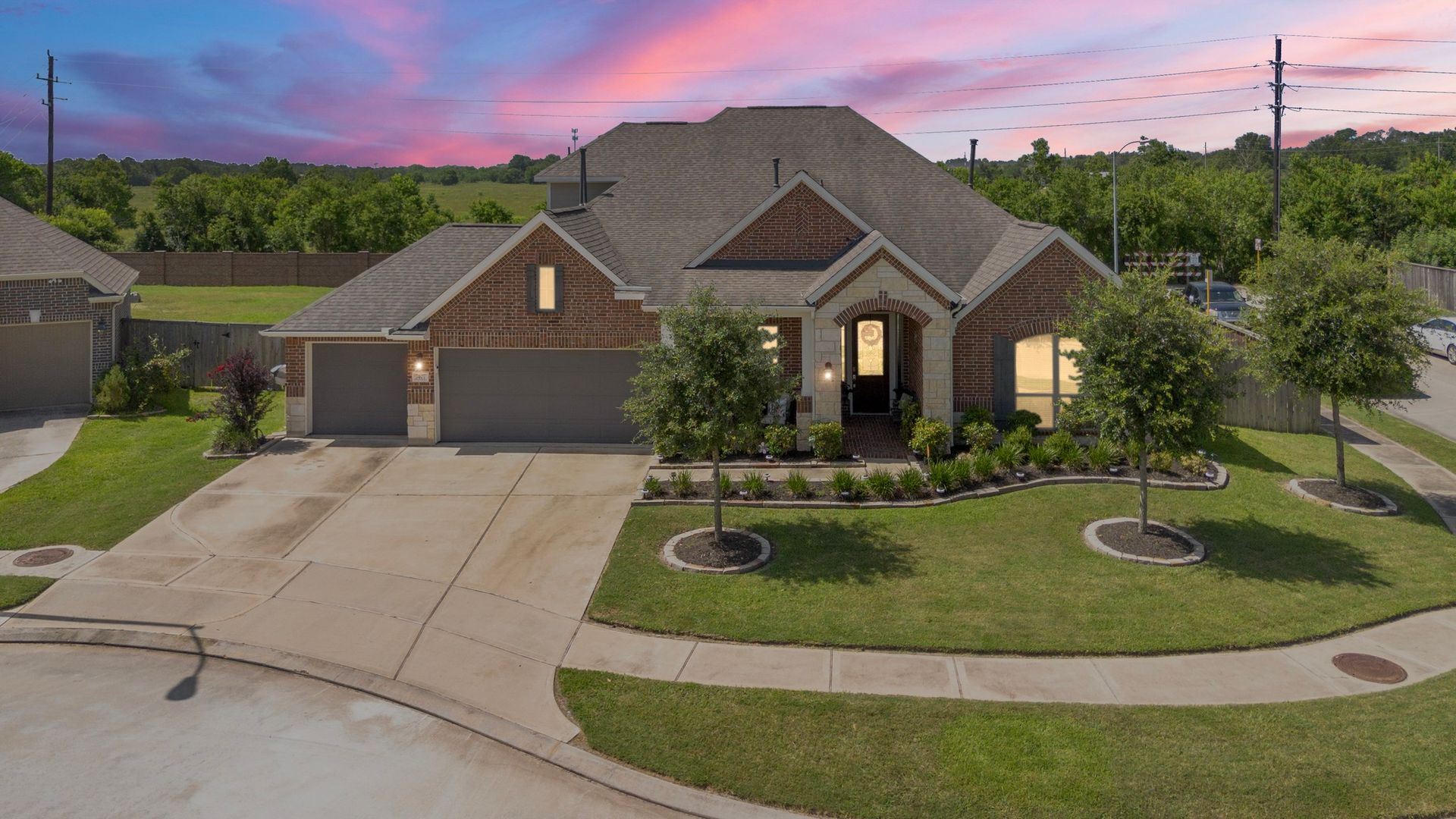 Brick single-story home at dusk with warm windows and a pink sky, photographed by JI Media Group