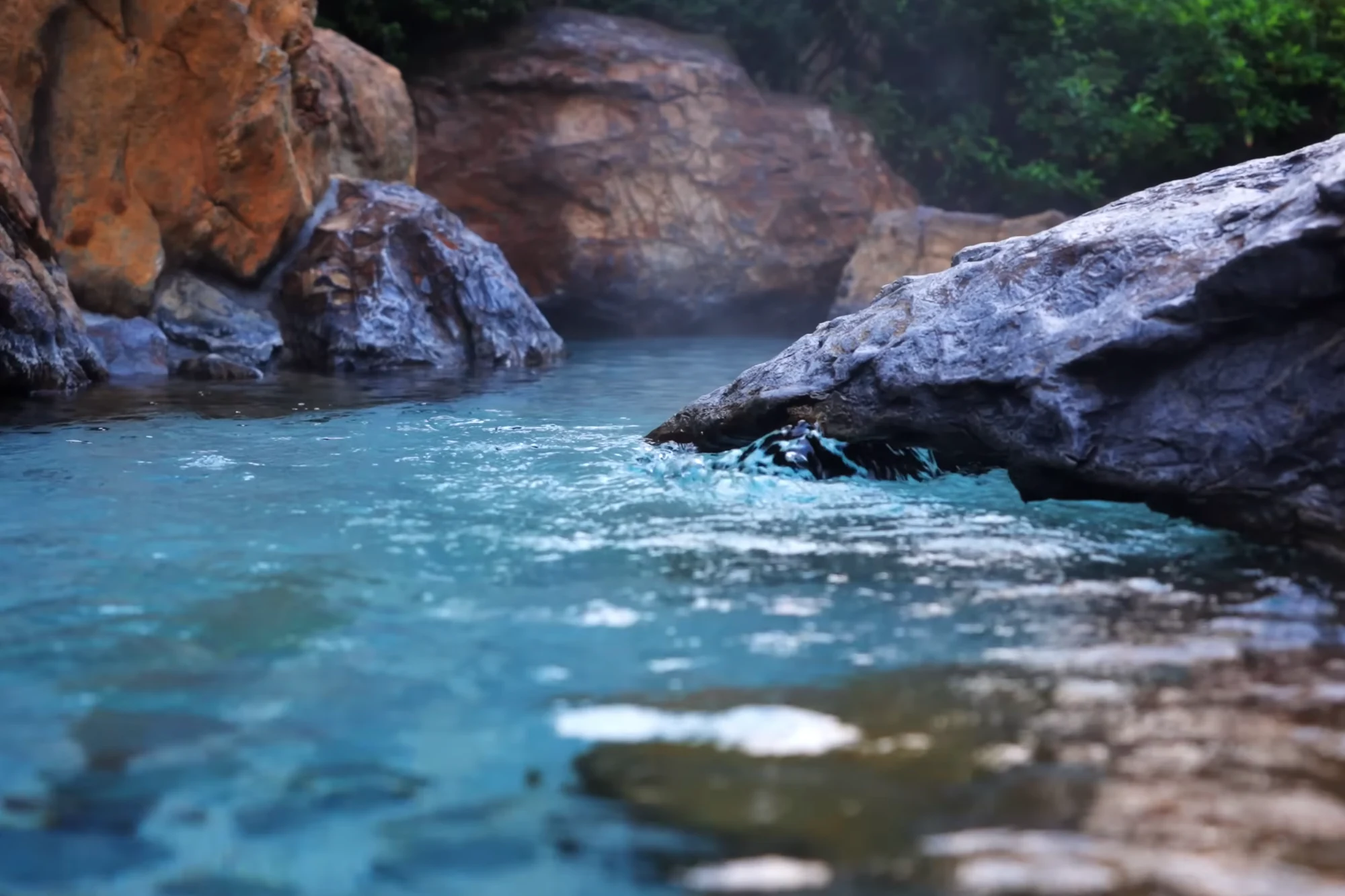 A turquoise river running between pale rock and forest near Kinosaki.