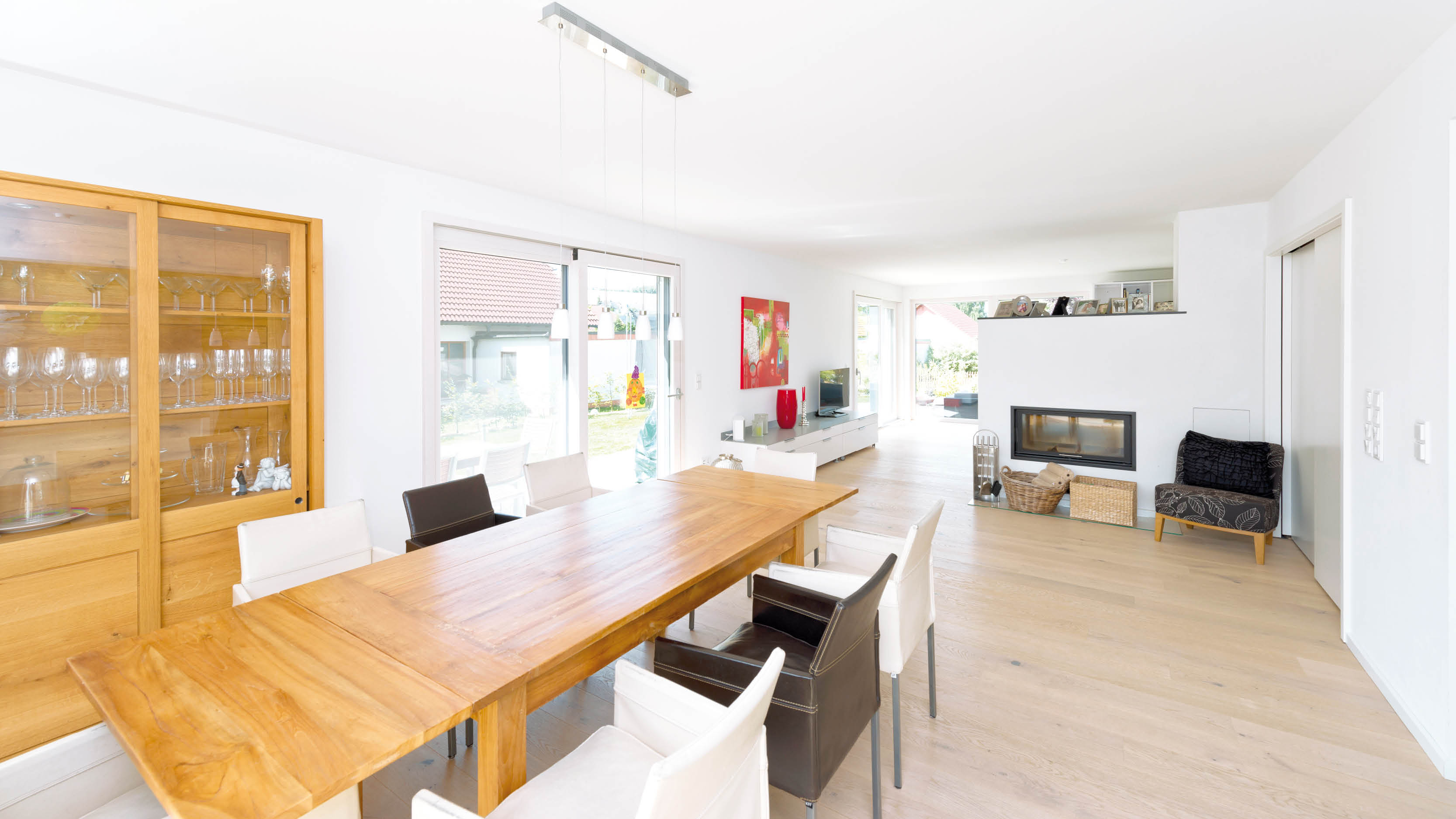 Helles Esszimmer mit Holztisch, Ledersesseln, Glasschrank und Kaminbereich.