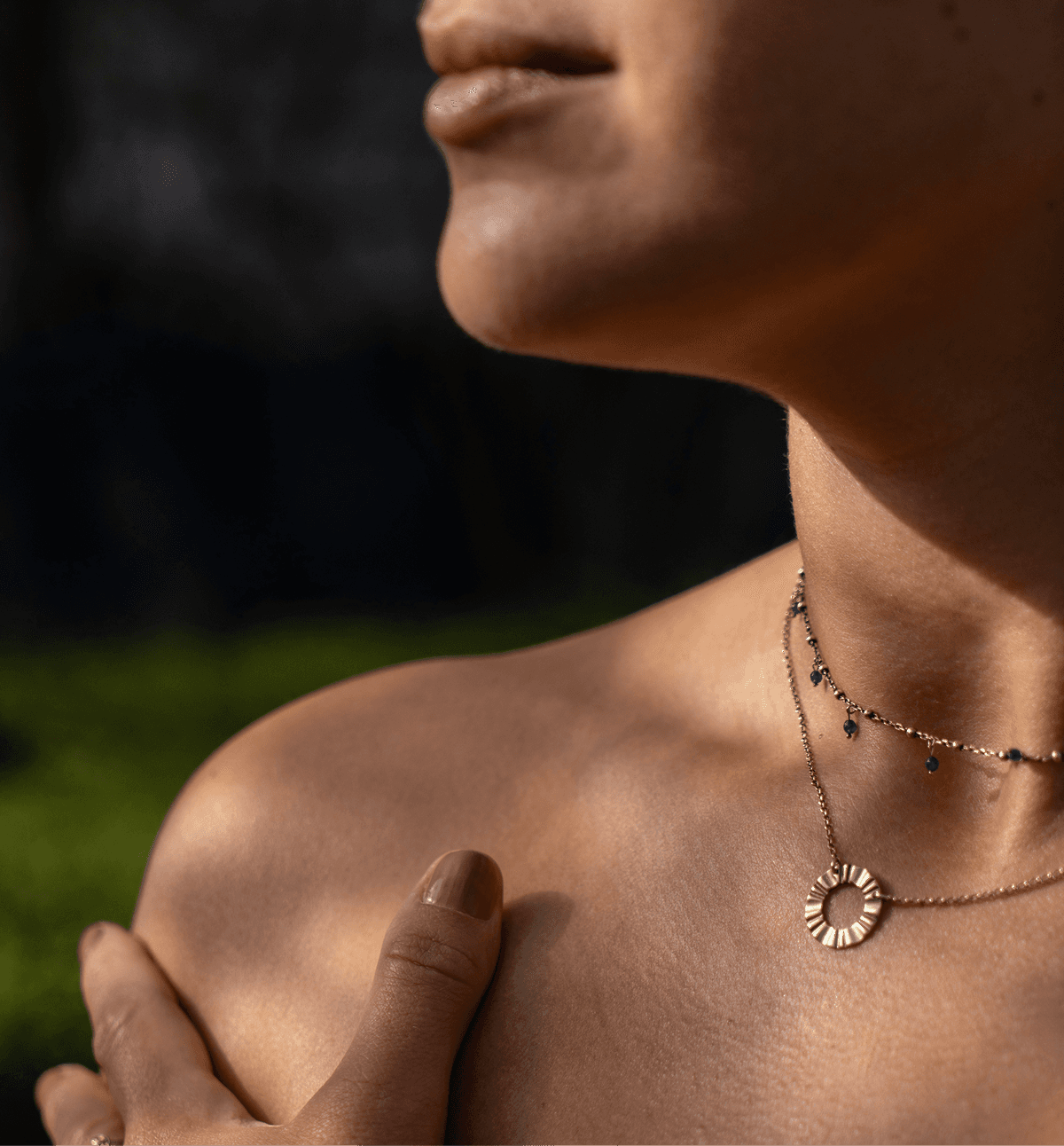 A serene close-up captures a person gently touching their shoulder, displaying a delicate necklace with a sun-shaped pendant, evoking a sense of calm and wellbeing.