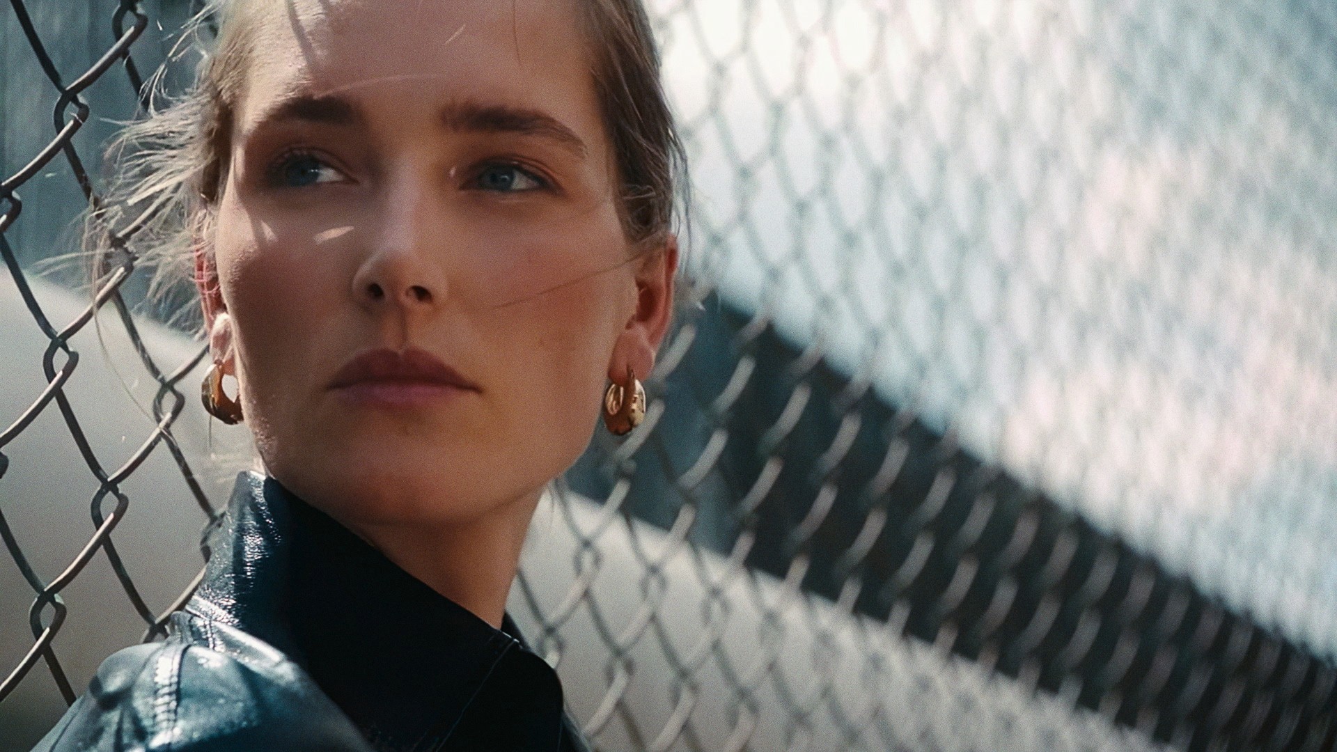 Close-up of a woman in black leather in front of a chain-link fence and sky, Lafayette 148 New York