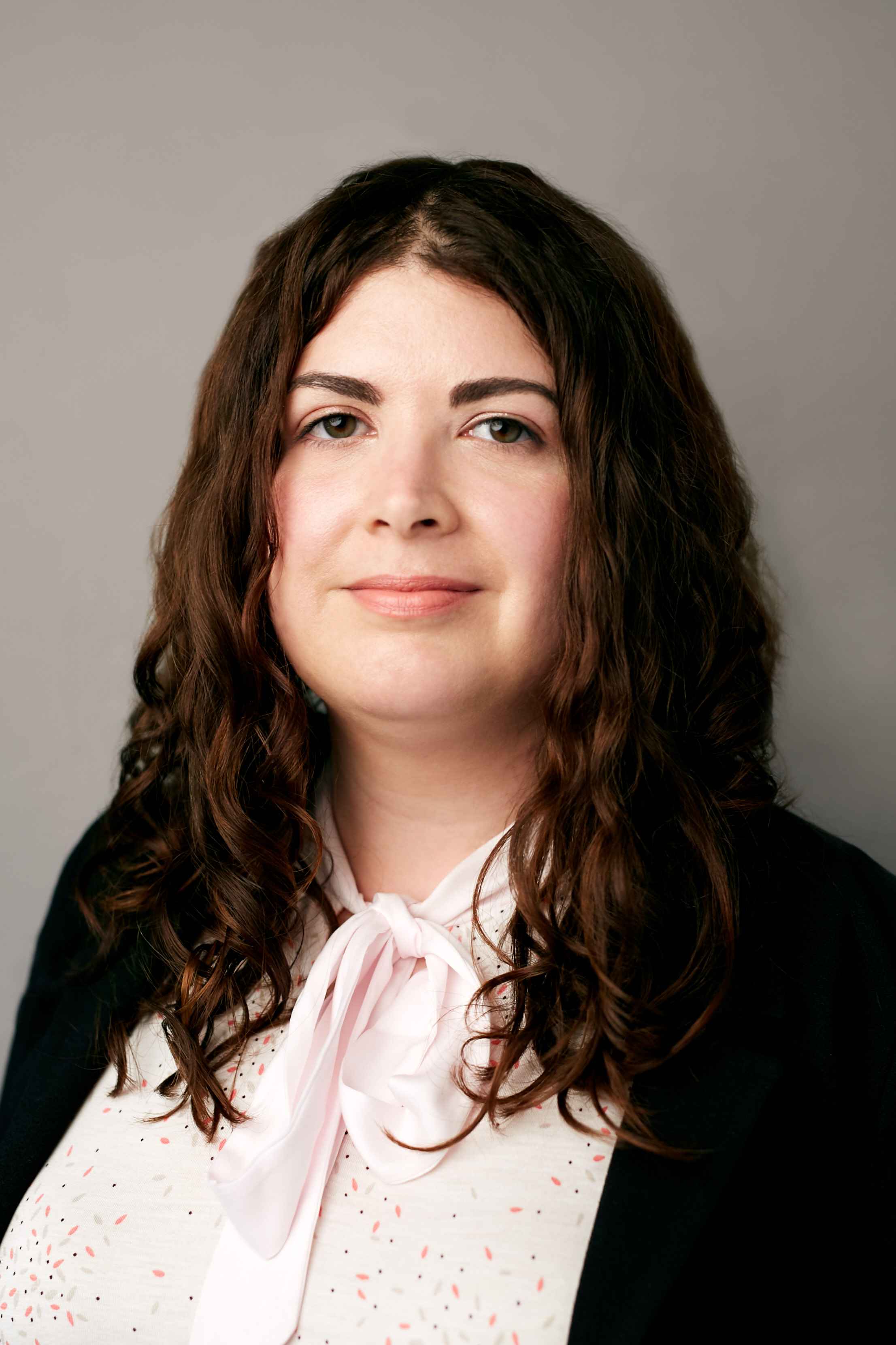 Woman with long, wavy brown hair and a pink bow tie.