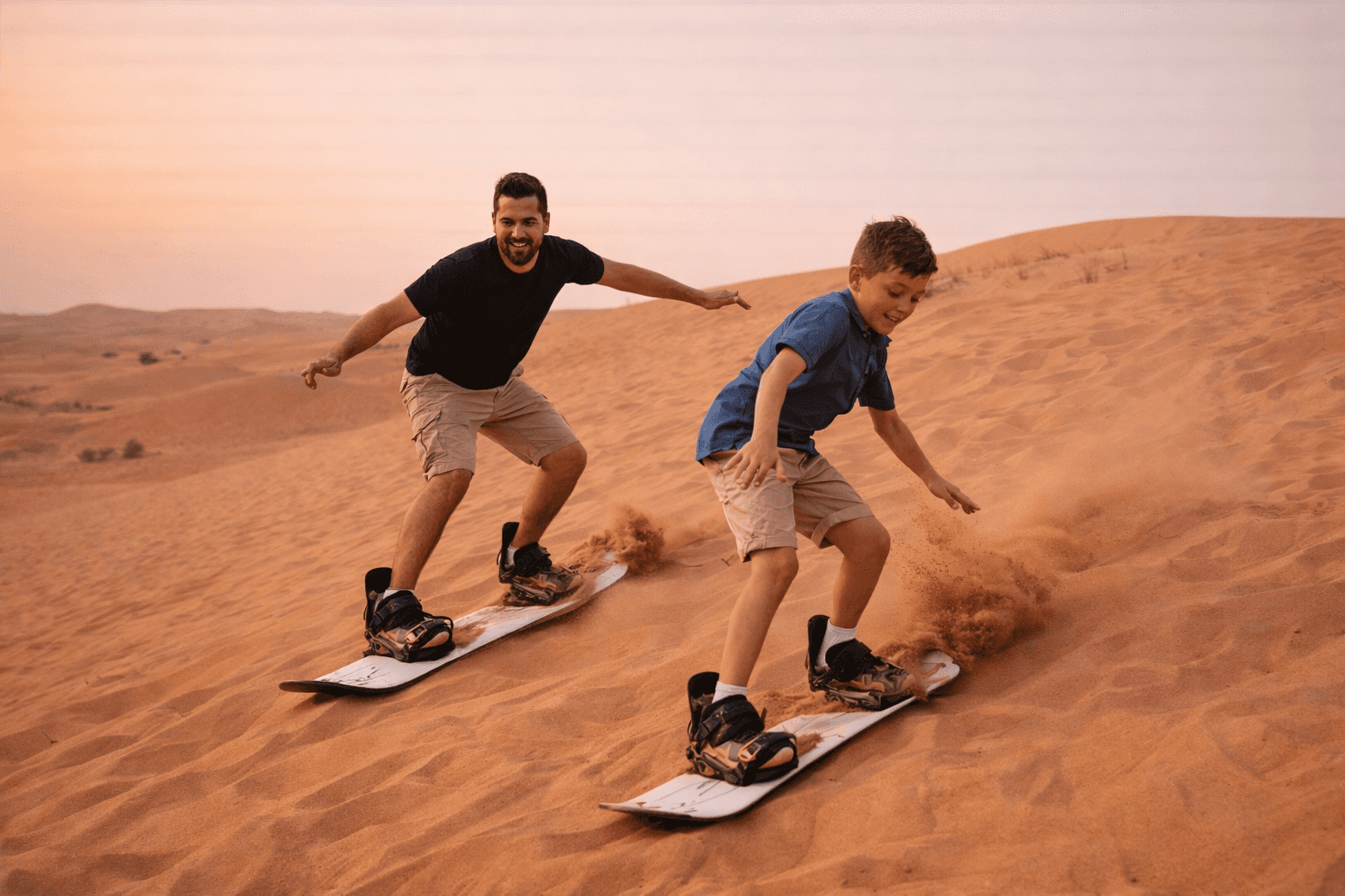 Father and son sandboarding during a private morning desert safari in Dubai with Dune Quest Tours