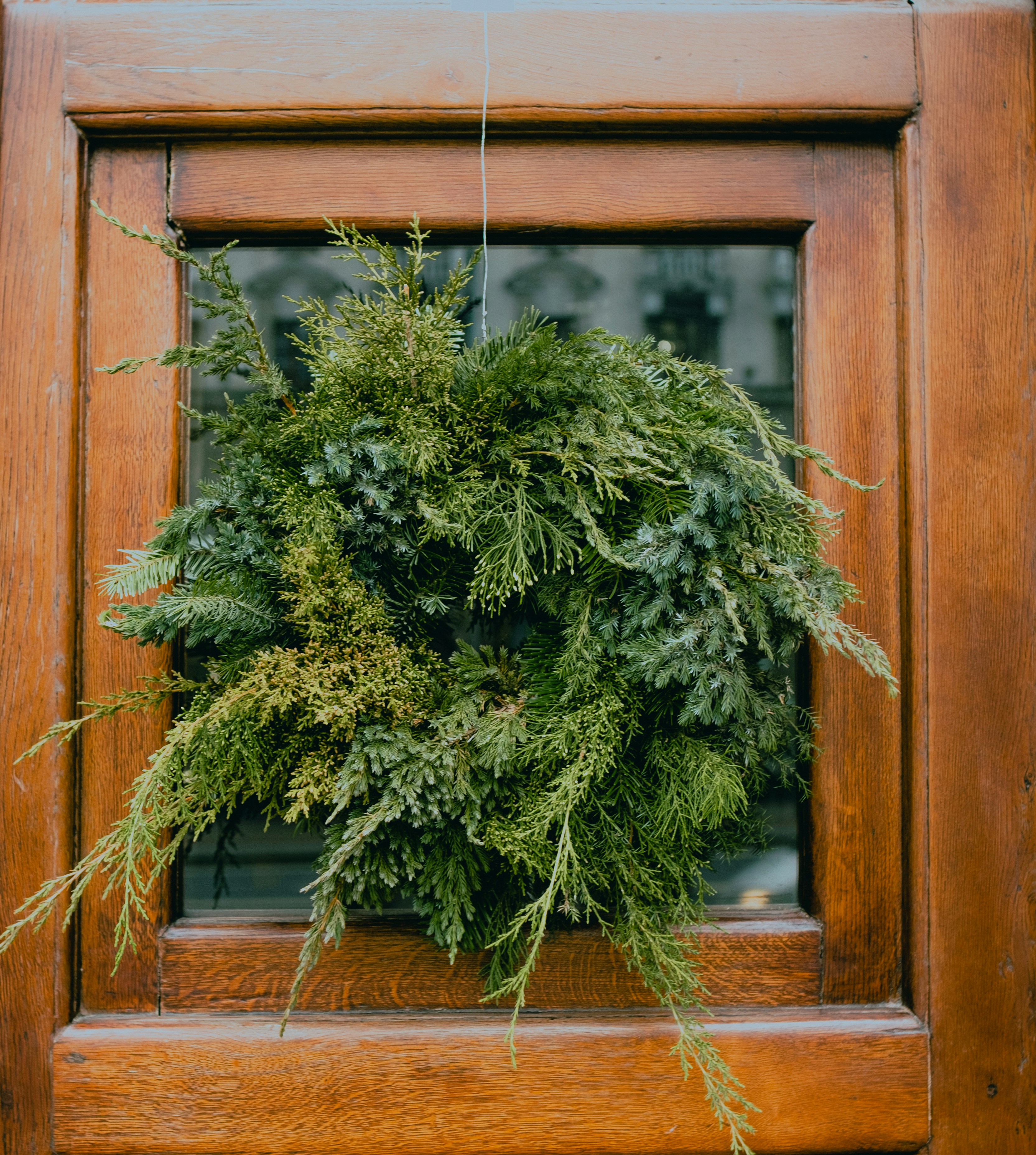 A lush green wreath hanging on a wooden door.