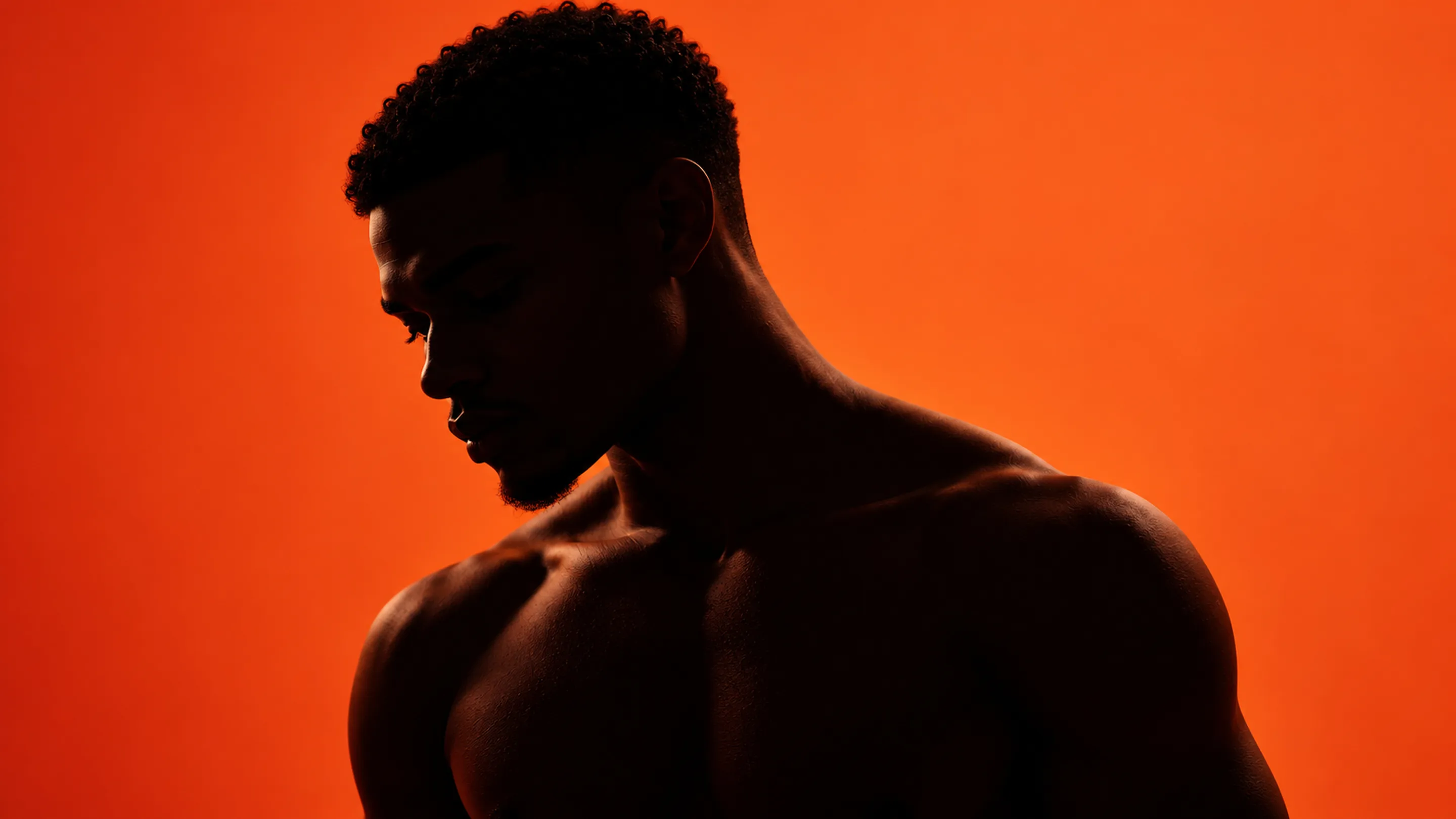 Man in silhouette looking down, lit from behind in orange