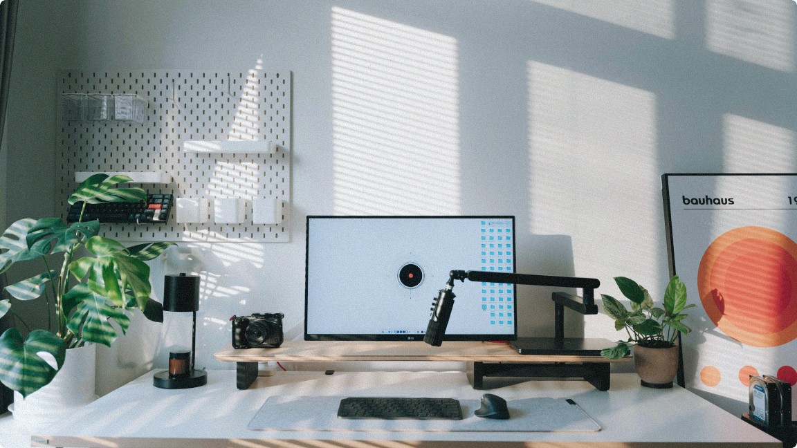 Heller Arbeitsplatz mit großem Monitor, ergonomischem Stuhl, Pflanzen und Accessoires im Sonnenlicht 