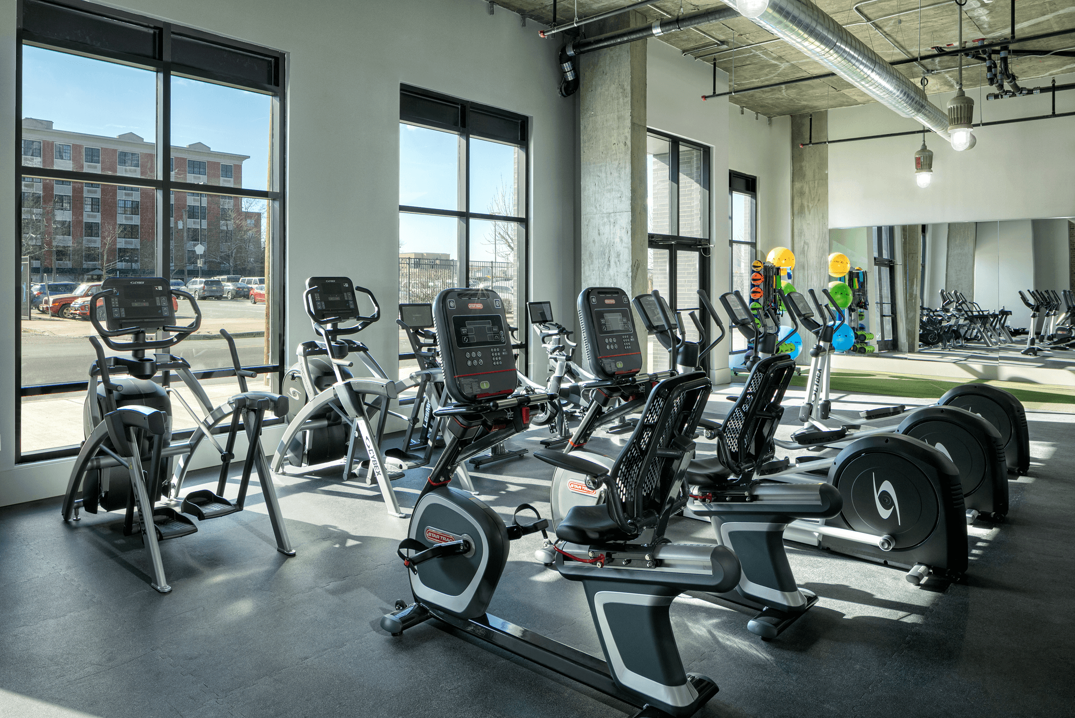 A modern gym interior featuring weightlifting equipment and large windows allowing natural light.