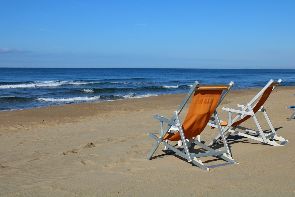 Two empty deck chairs facing calm surf on a wide sand beach in shoulder season