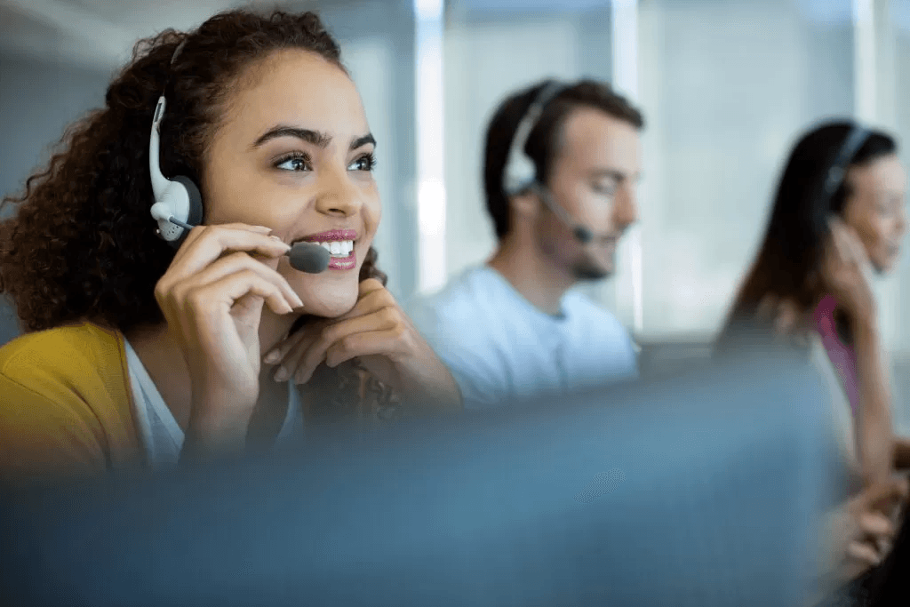 Image of a lady talking on a headset, with other workers in the background.