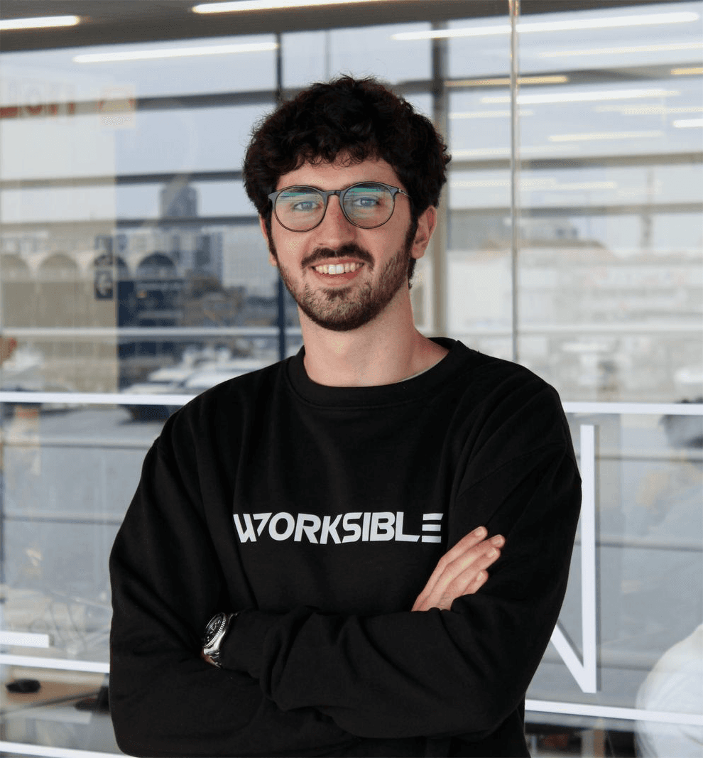 Smiling man with glasses giving a thumbs up while seated at a laptop in natural light