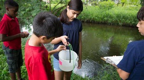 High school students exploring environmental research during summer programs like RISE; outdoor STEM activity studying water ecosystems, data collection by stream.