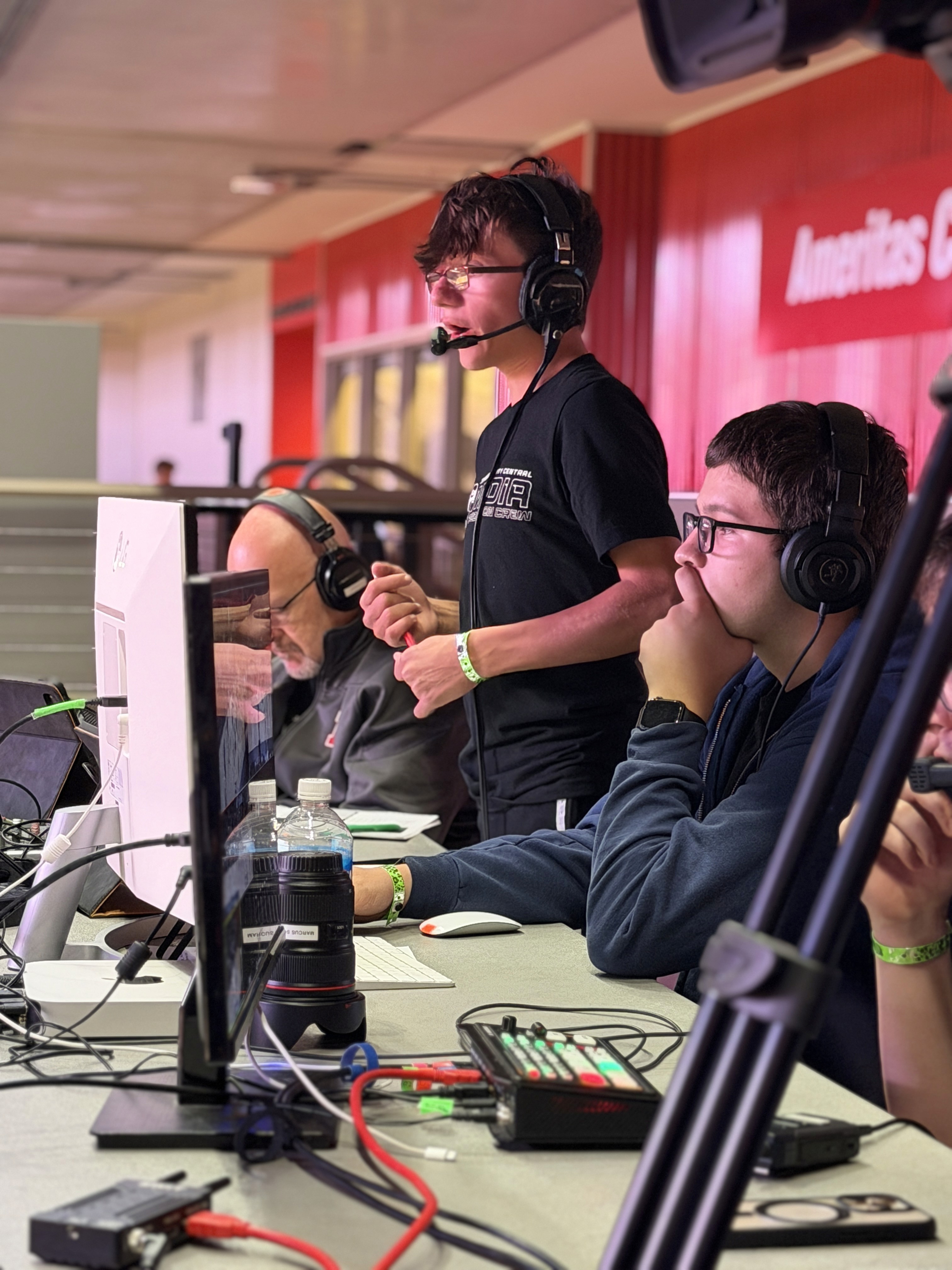 Student announcers and production crew working at a broadcast desk during a state basketball tournament