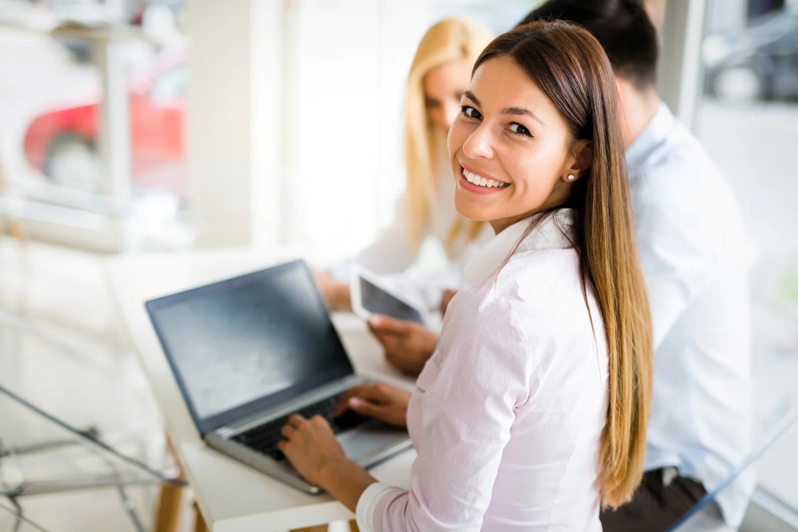 Smiling professional working on her laptop with colleagues nearby
