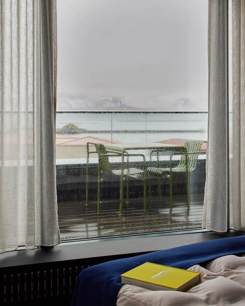 Rainy harbour-facing windows with curtains and a lounge chair.