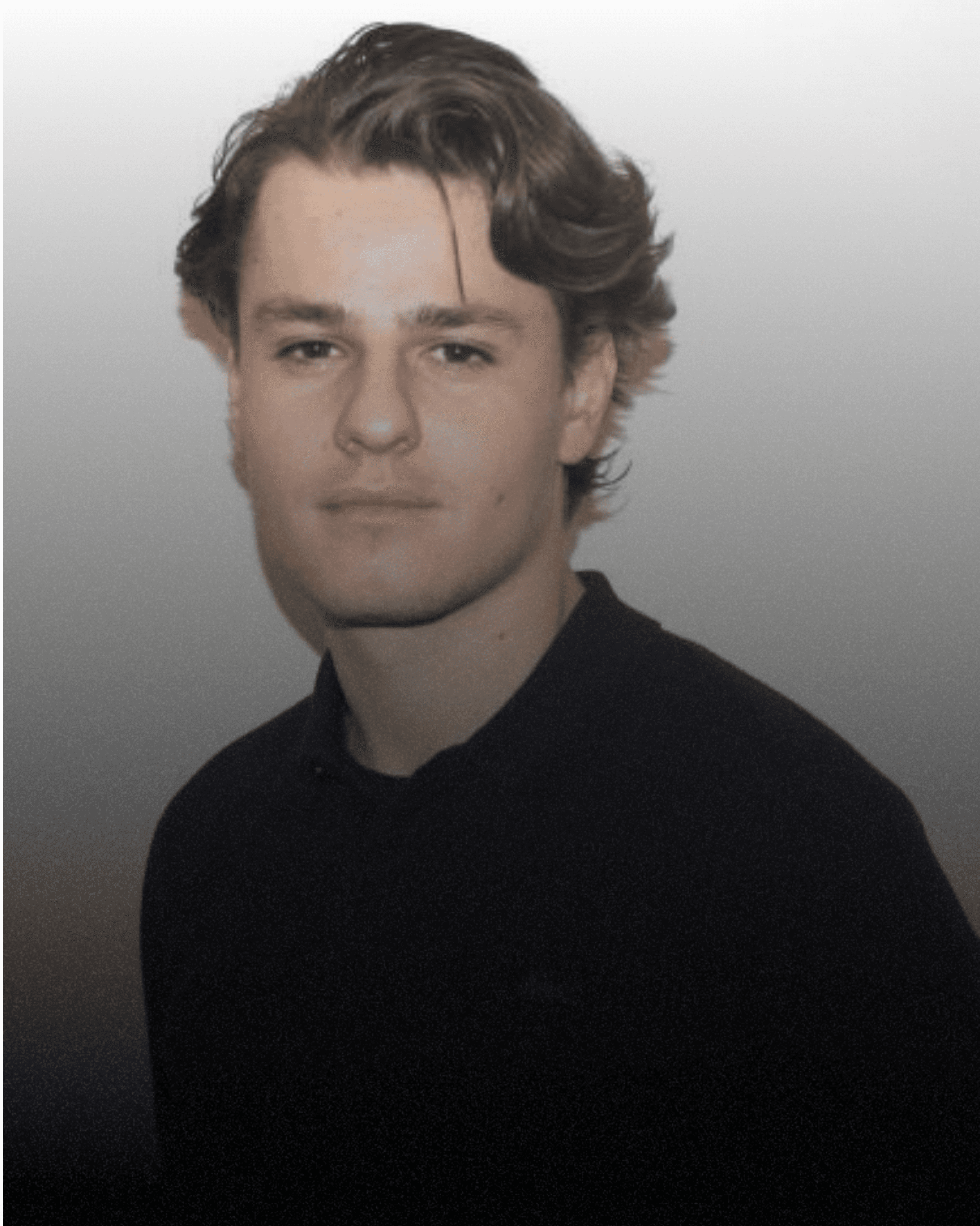 A portrait of a young woman with long, wavy brown hair wearing a mauve knitted sweater and a ring, posing against a light-colored ribbed wall.