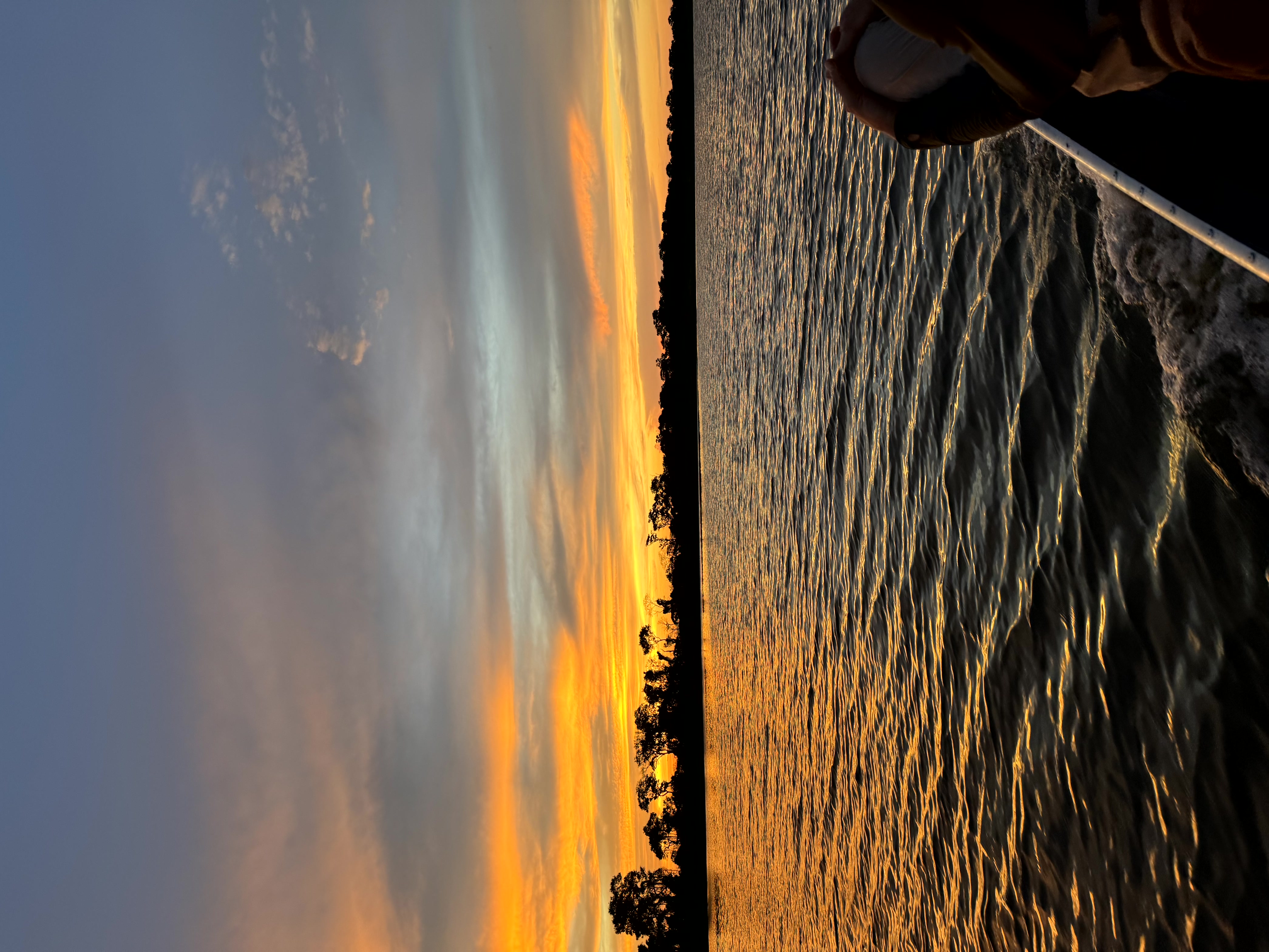 Sonnenuntergang auf dem Rio Paraguai im Pantanal – goldorangefarbenes Licht spiegelt sich auf dem Wasser, im Vordergrund ein Mensch auf einem Boot, am Horizont die dunkle Silhouette des Waldes.