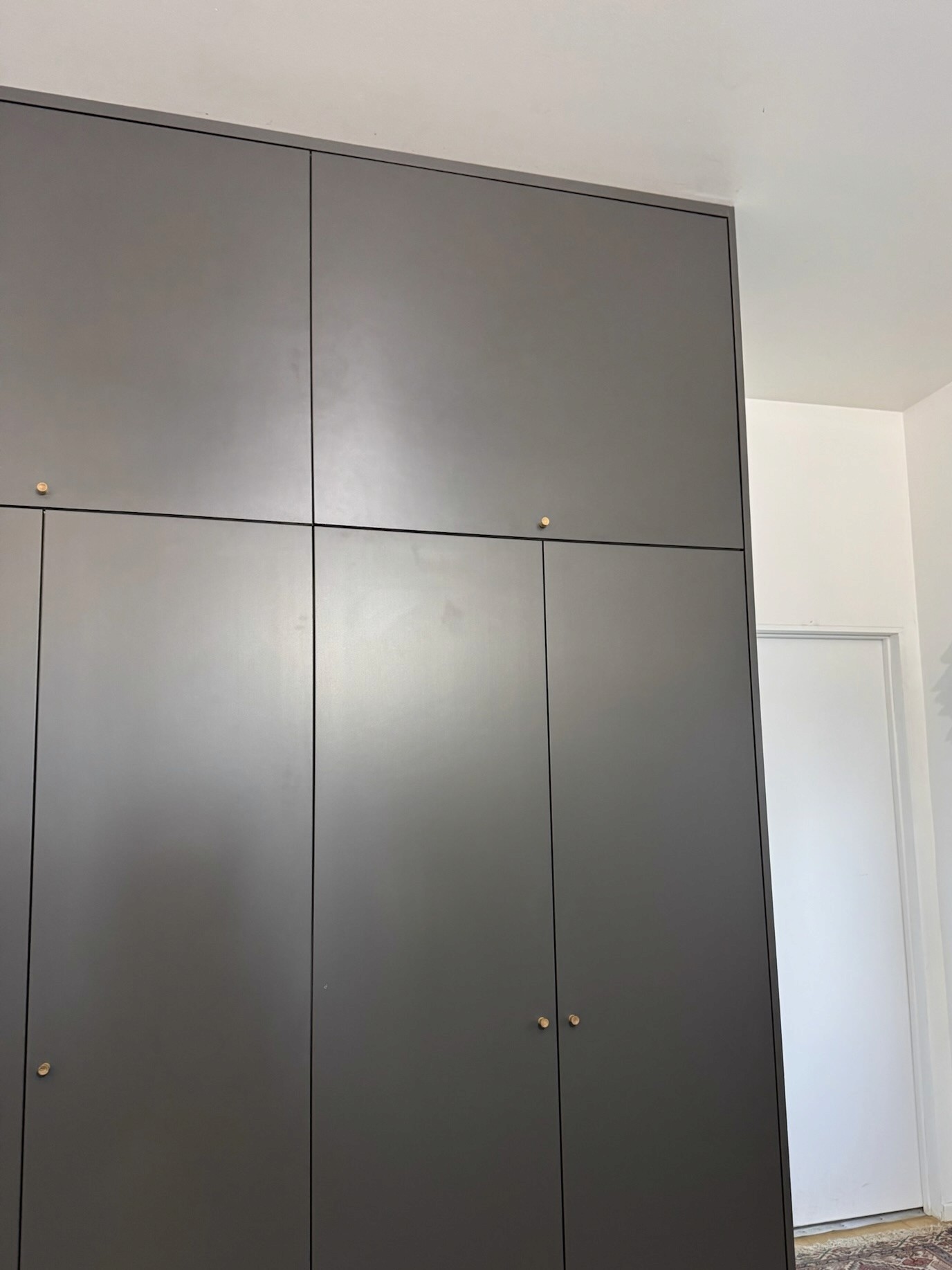 Floor-to-ceiling charcoal cabinetry with small brass knobs