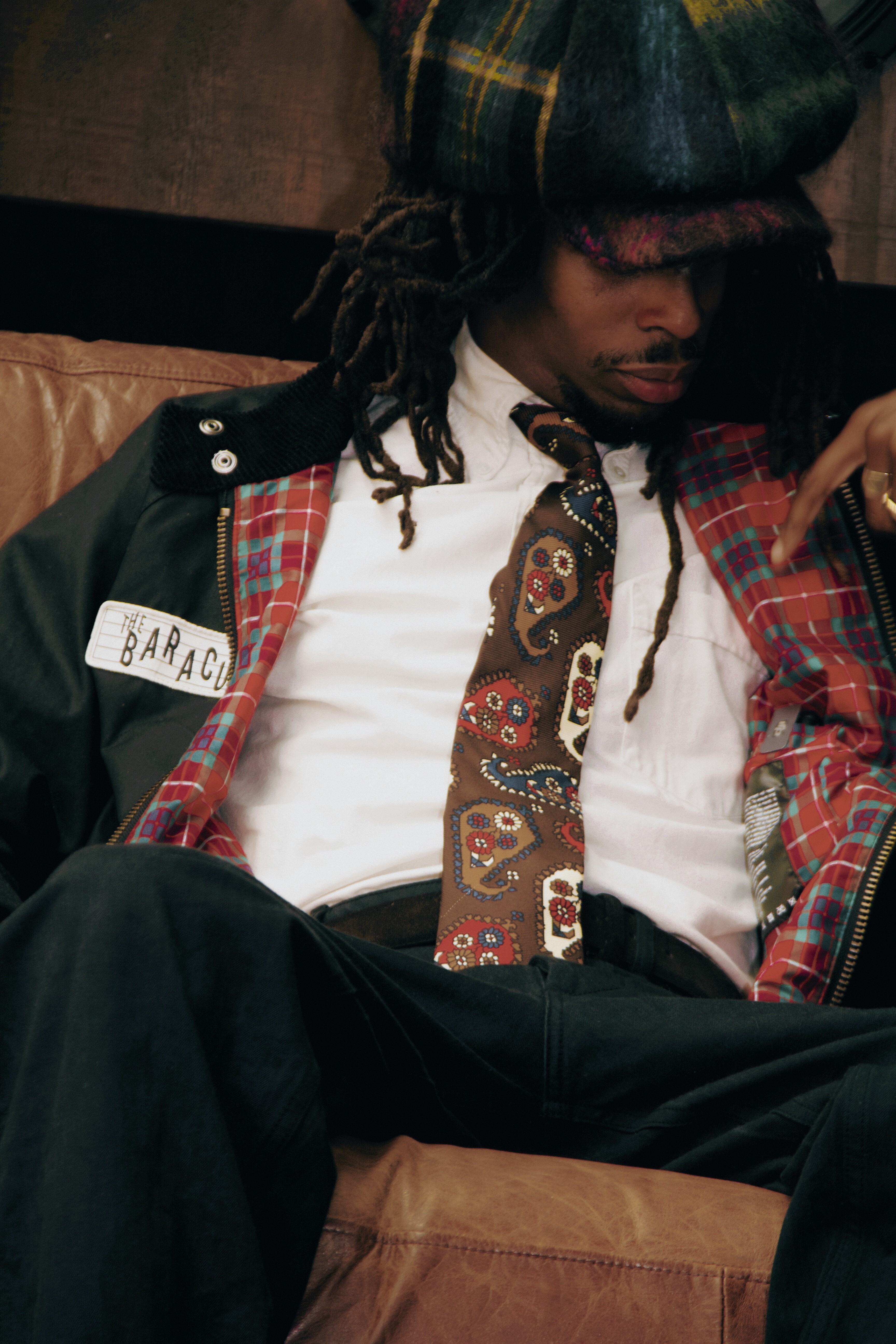 Dans le lookbook de la 3e collab Baracuta x Barbour, un chanteur porte un blouson de pluie marine avec doublure en tartant, chemise blanche et cravate dans un look rappelant la scène Northern Soul