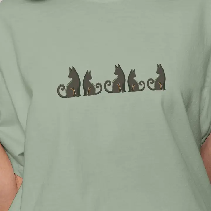 Row of black cats painted on a sage tee